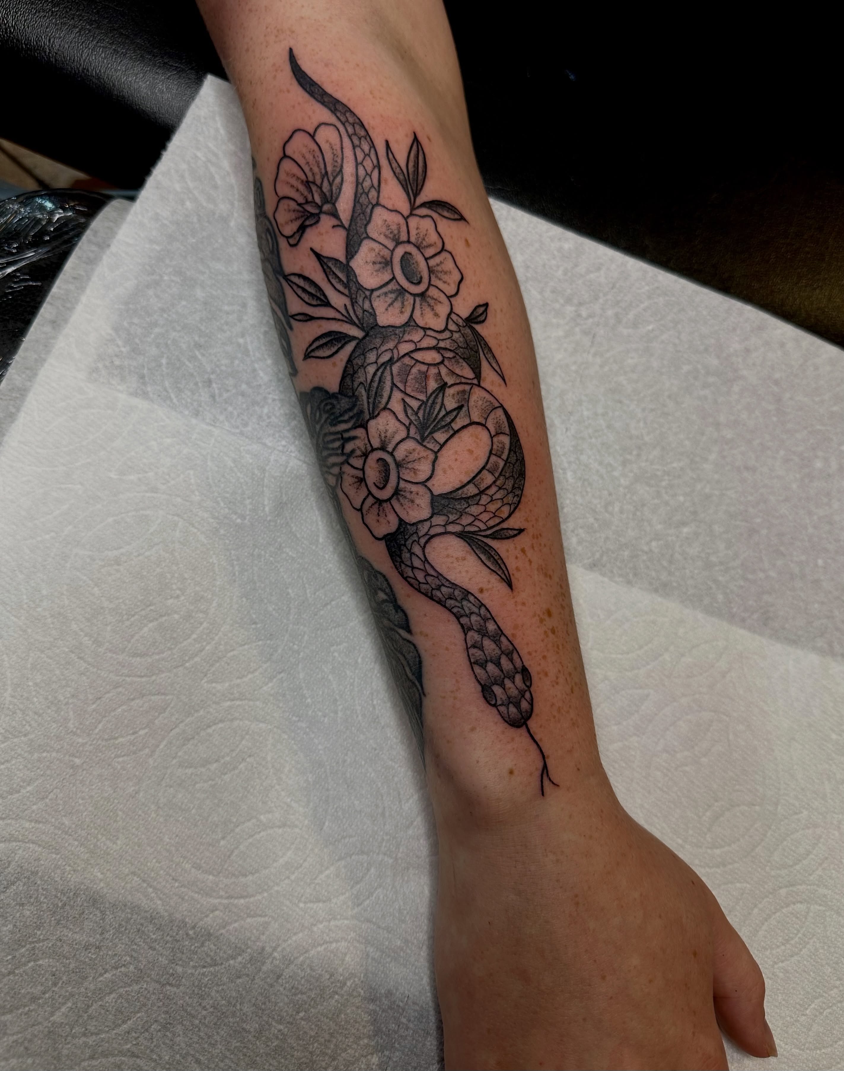 Snake and flowers black and grey tattoo on the forearm by teddy, Portland, Oregon
