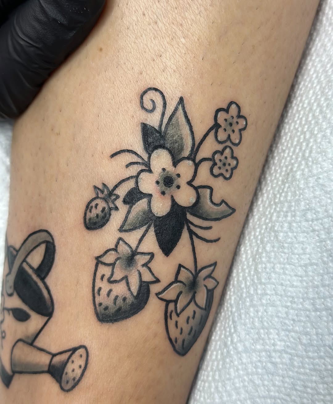Strawberries and flowers with watering can ignorant tattoo on the forearm by Lucy Jay