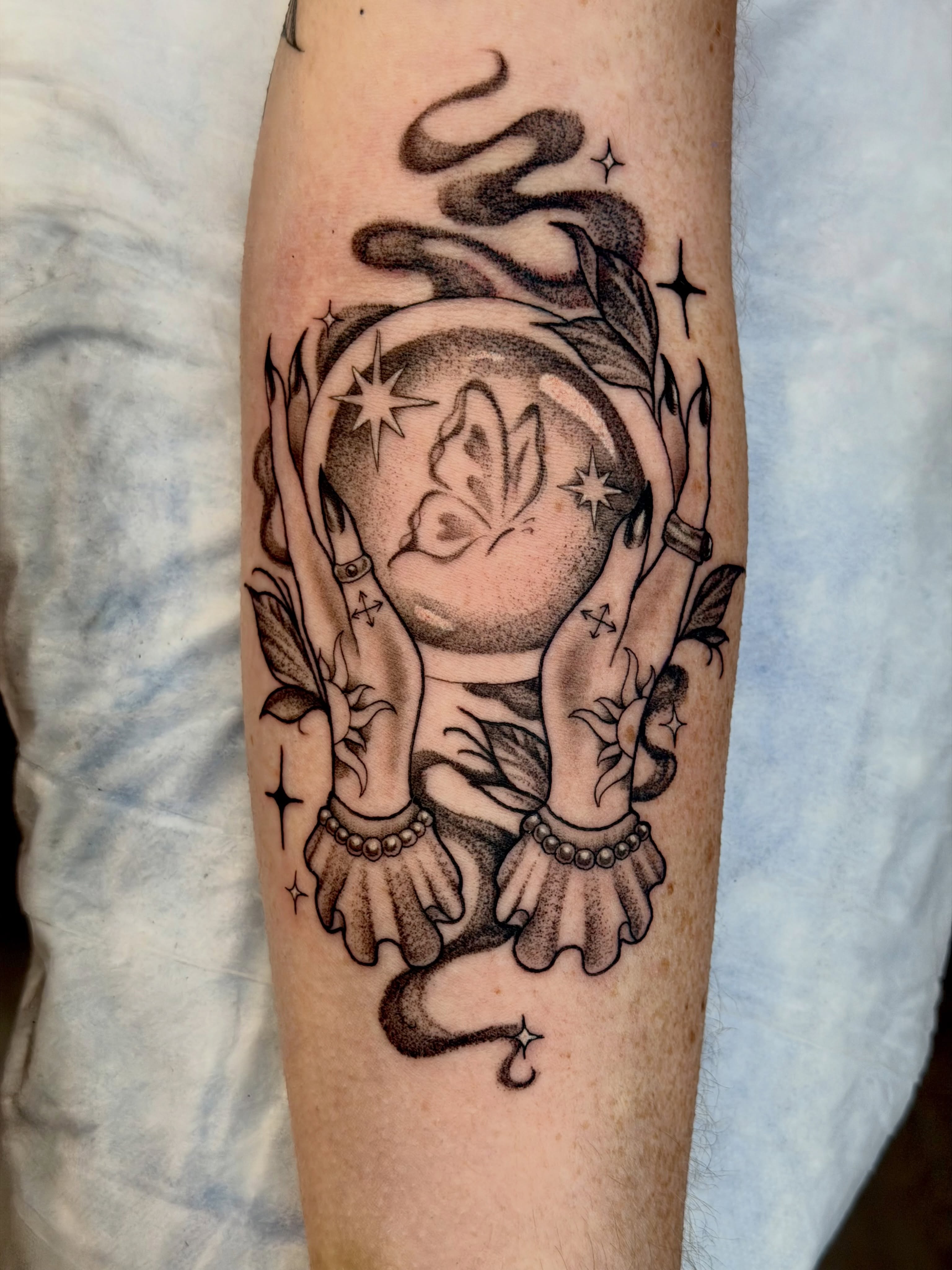 Crystal ball with butterfly black and grey tattoo on the forearm by Caitlynn Austin