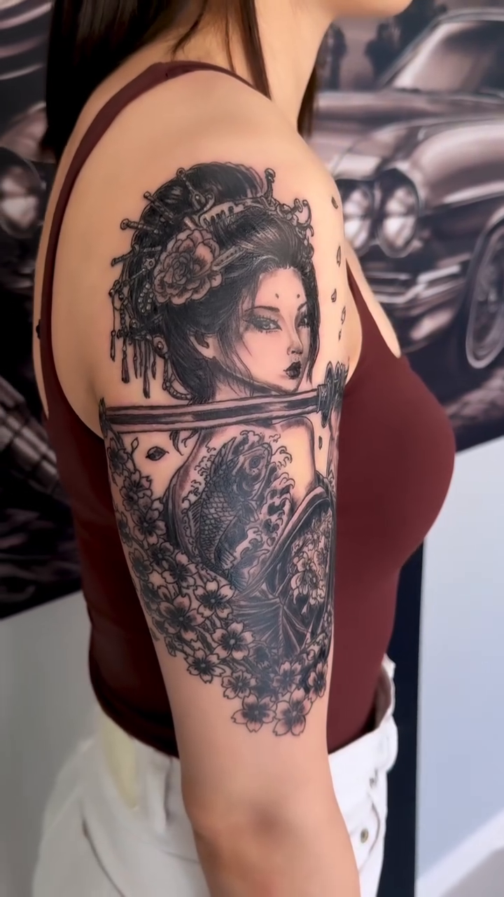 Geisha with fan and koi realism tattoo on the upper arm by Salvador Mendoza, Sesto San Giovanni