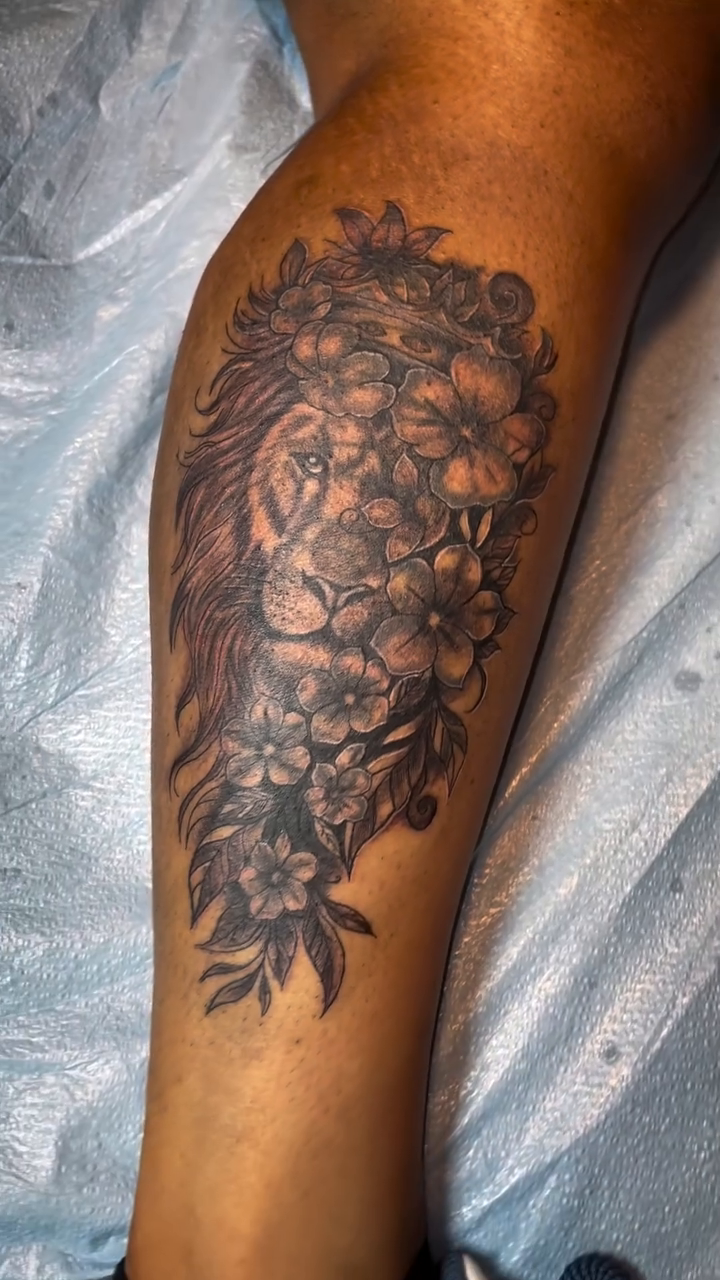 Lion head with floral wreath realism tattoo on the leg by The Reelist Ink