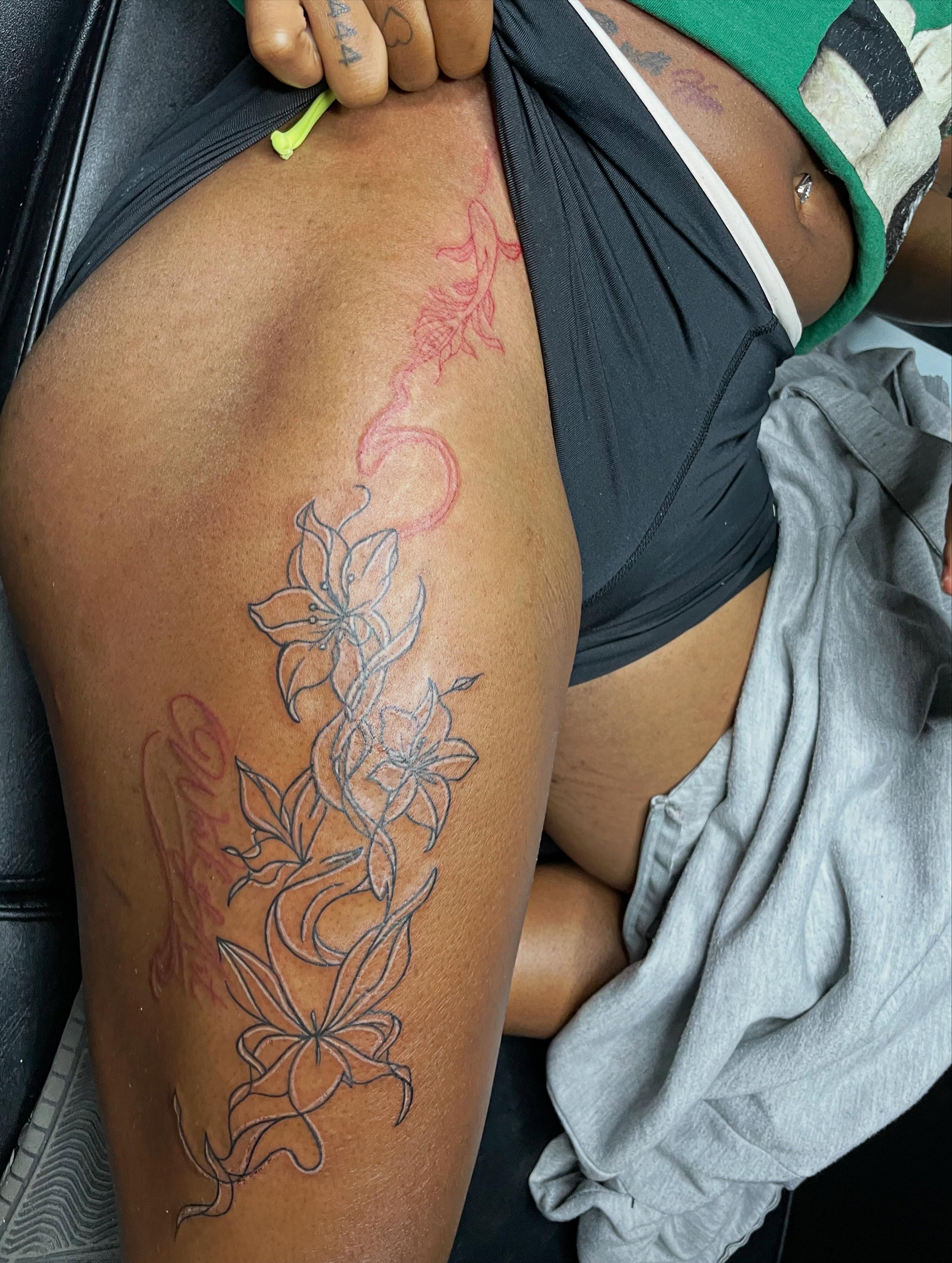Lilies and script black and grey tattoo on the thigh by TreCashTats💉🩸 MisfitzTattooStudio
