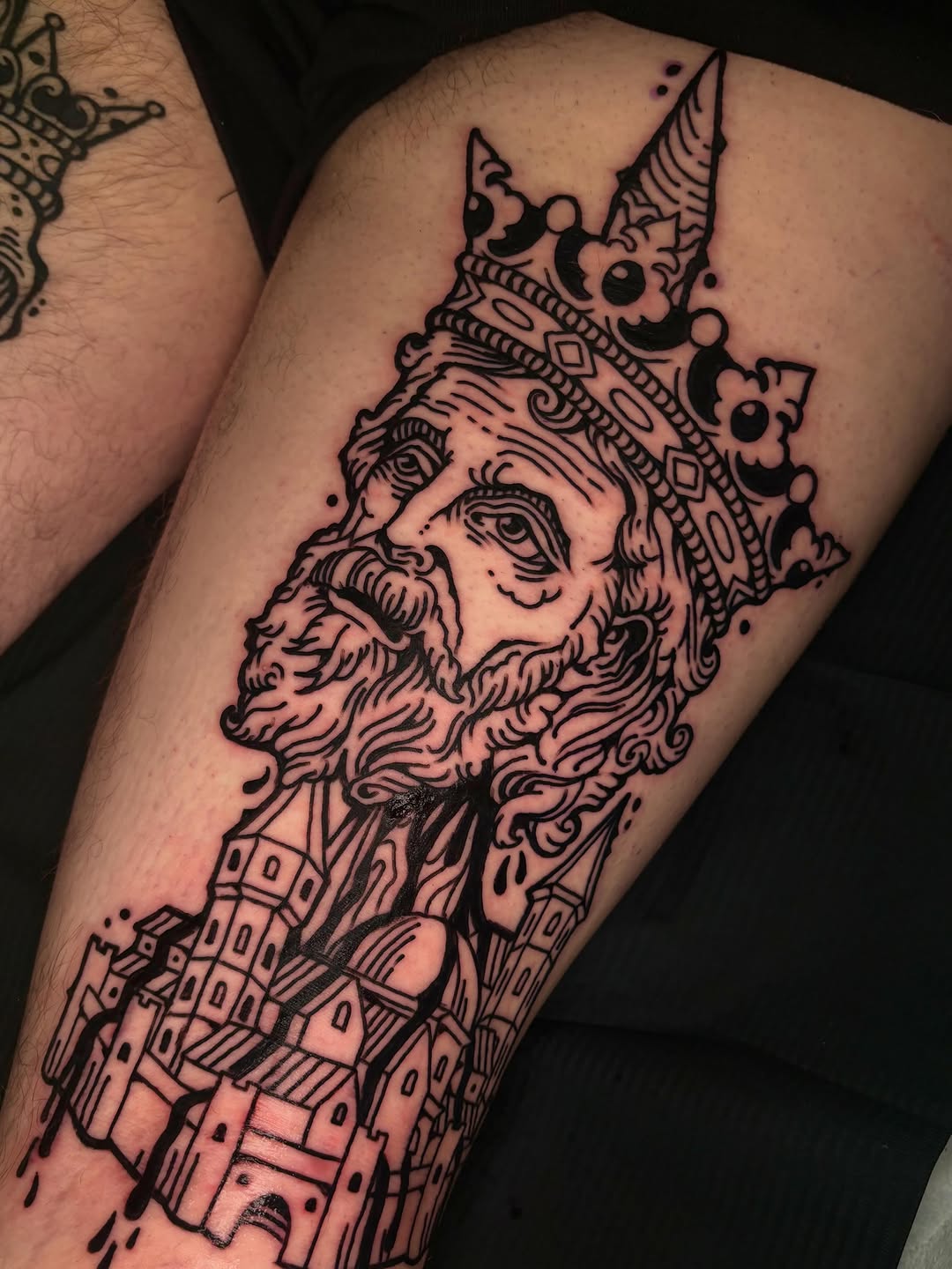 King's head with a city dark art tattoo on the thigh by 𝕵𝖊𝖗𝖊𝖒𝖞 𝕻𝖚𝖗𝖈𝖊𝖑𝖑