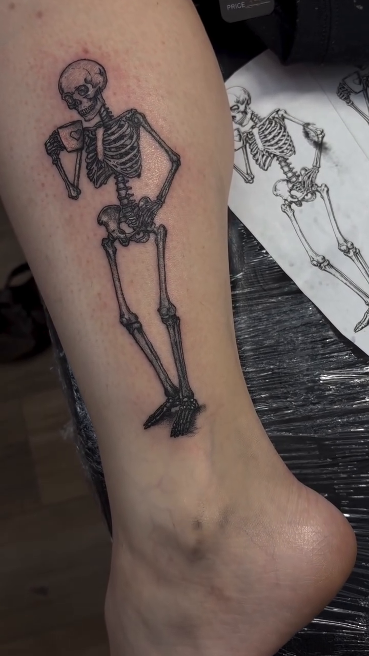 Skeleton holding a coffee cup sketch tattoo on the leg by Mike Tatts