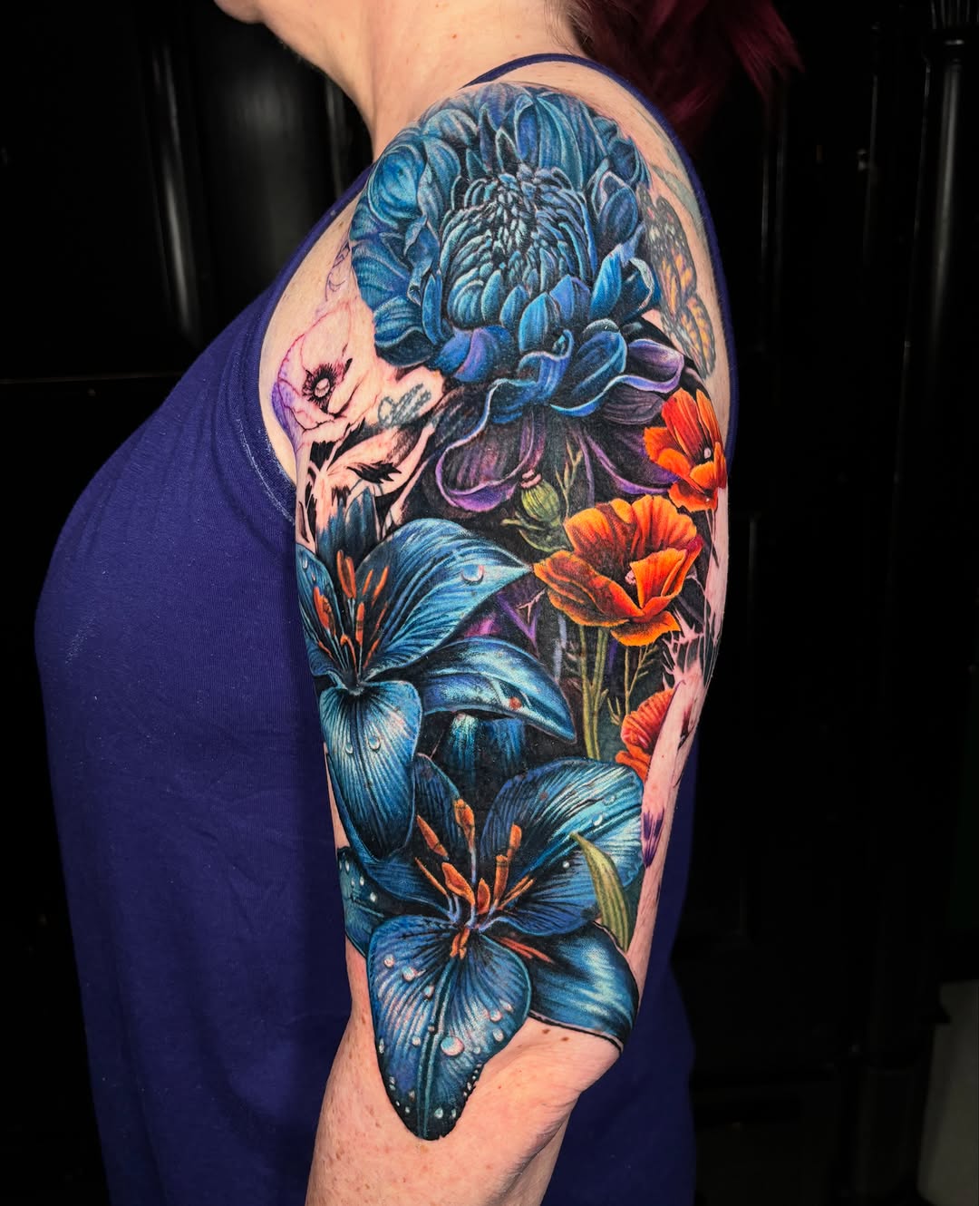 Blue lilies and orange poppies watercolor tattoo on the upper arm by Jon Ronzka