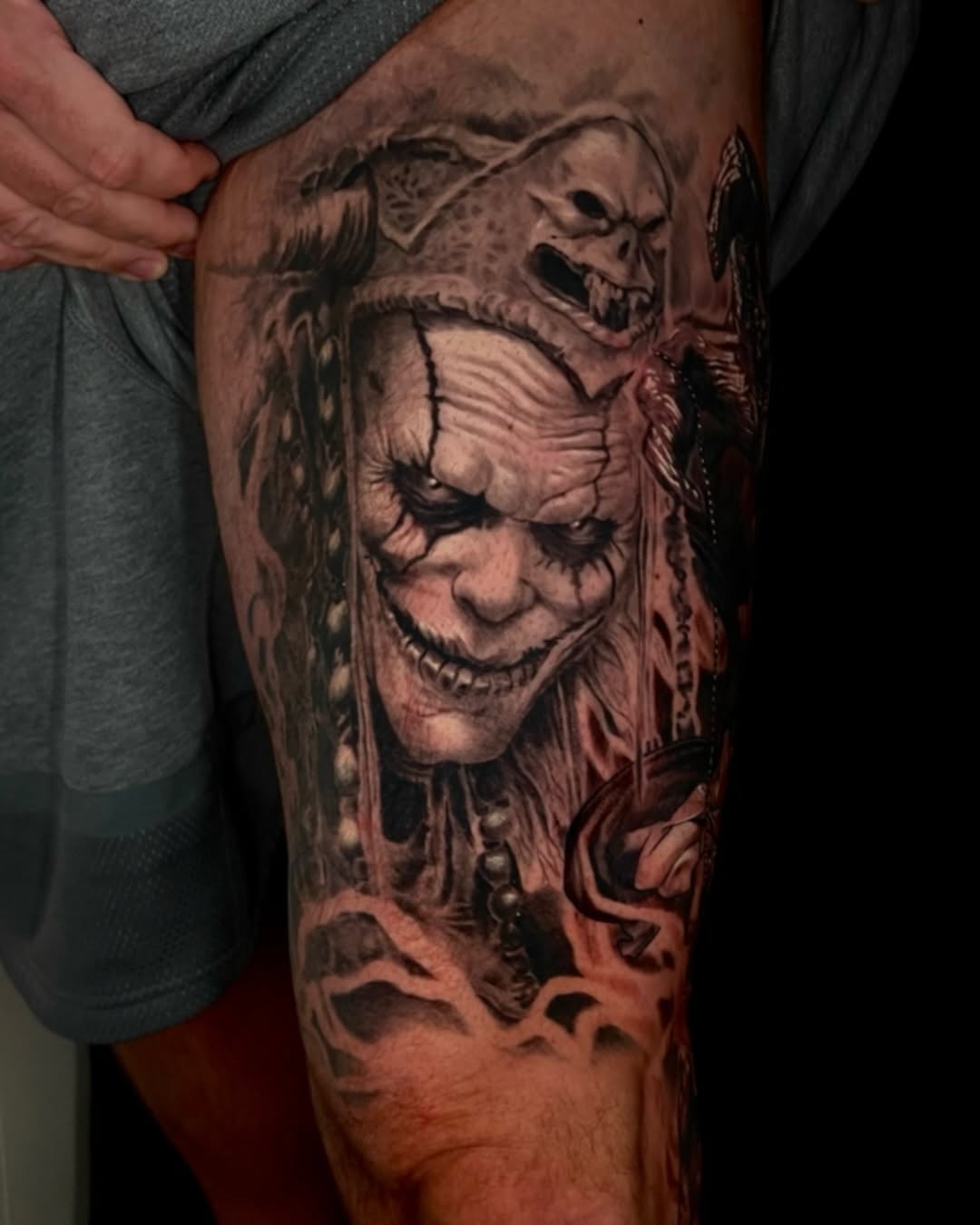 Creepy clown with skull headdress realism tattoo on the thigh by Tattoo Artist