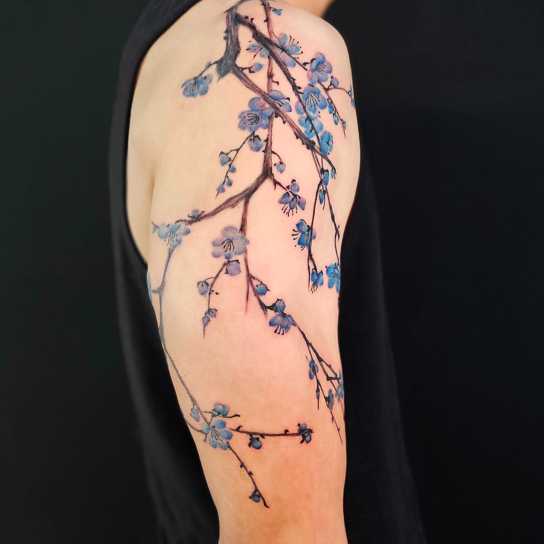 Cherry blossom branch watercolor tattoo on the upper arm by Lili Gu