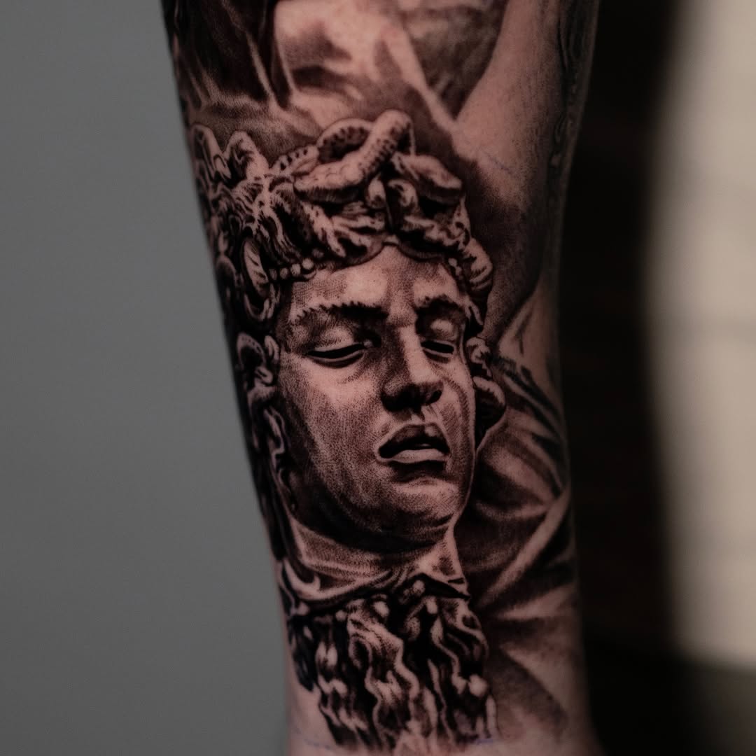 Medusa head statue surrealism tattoo on the forearm by Mark Vata
