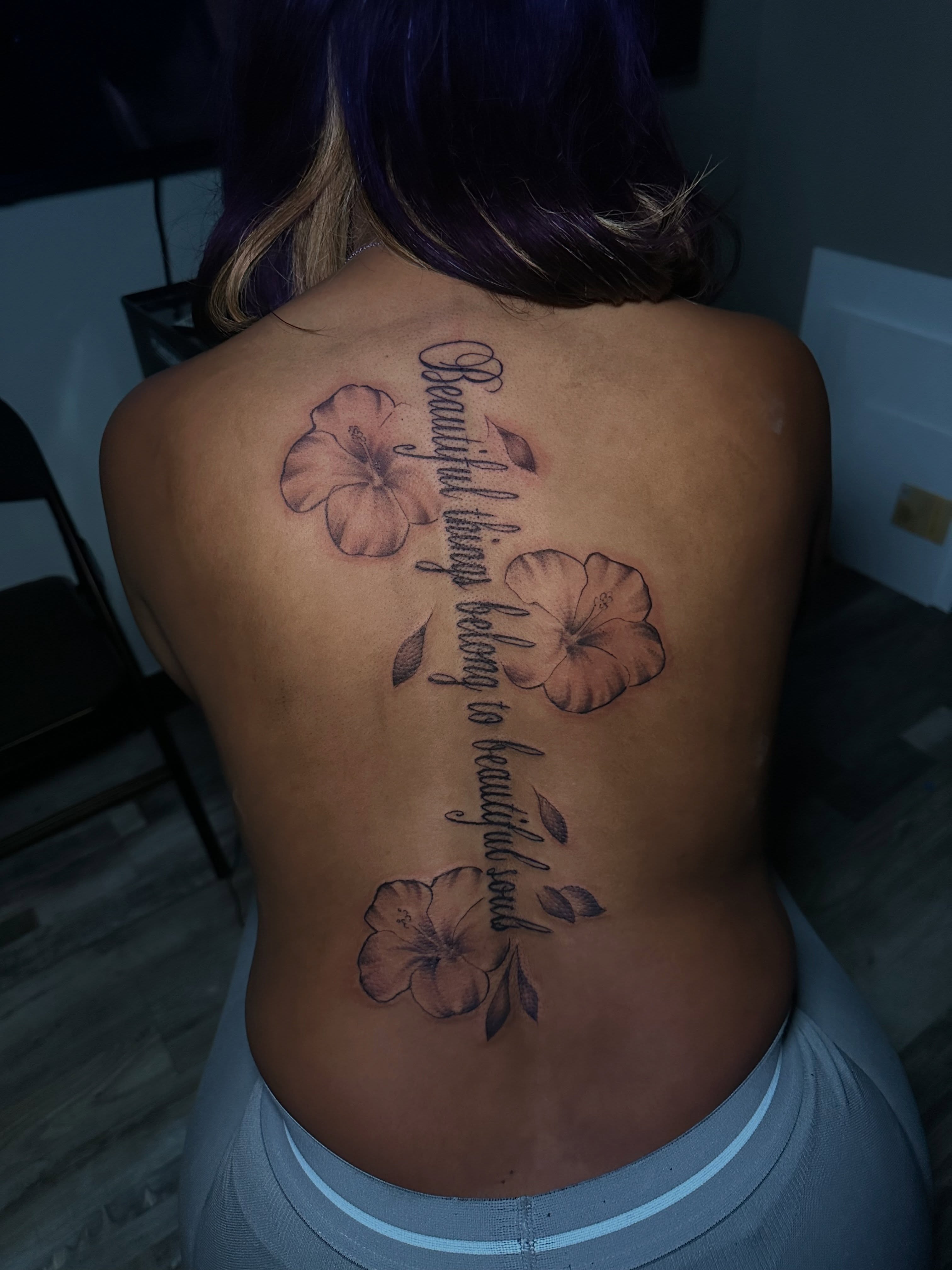 Flowers and script black and grey tattoo on the back by @tattedbytuck