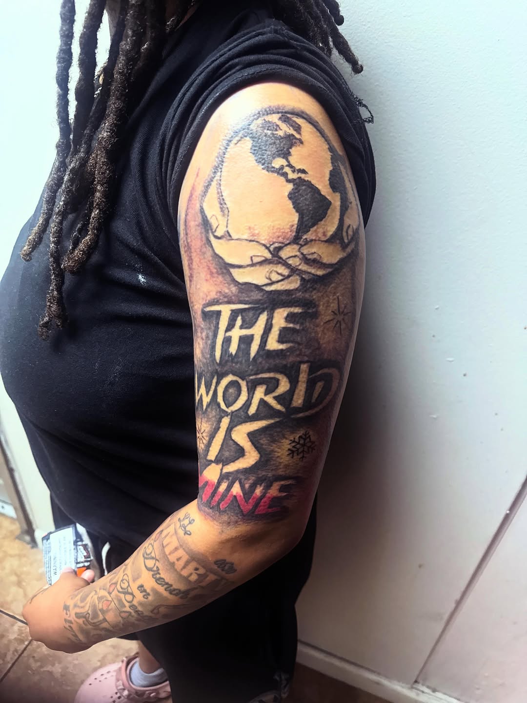 Hands holding globe with text tattoo on the upper arm by Uncle Fade Tattoo Artist ✍🏾