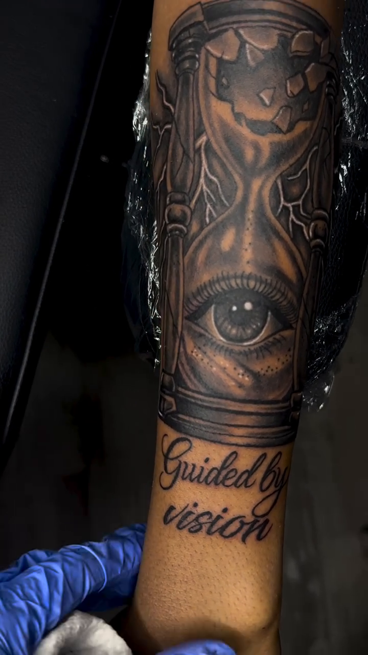 Hourglass with eye and script surrealism tattoo on the forearm by Left My Mark