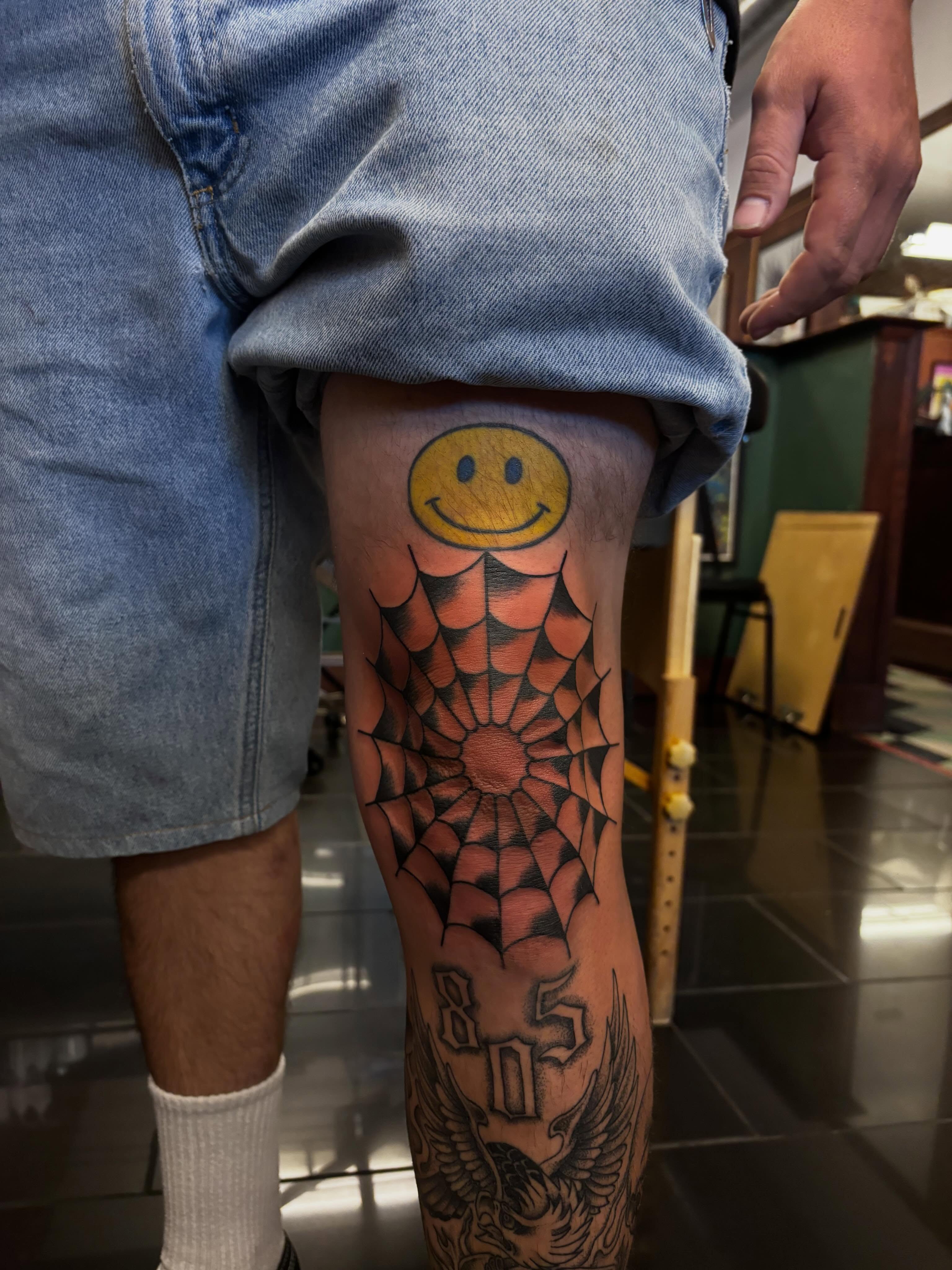 Smiley face with spiderweb American traditional tattoo on the thigh by Alyssa L'Heureux🕴🏼, Los Angeles, California