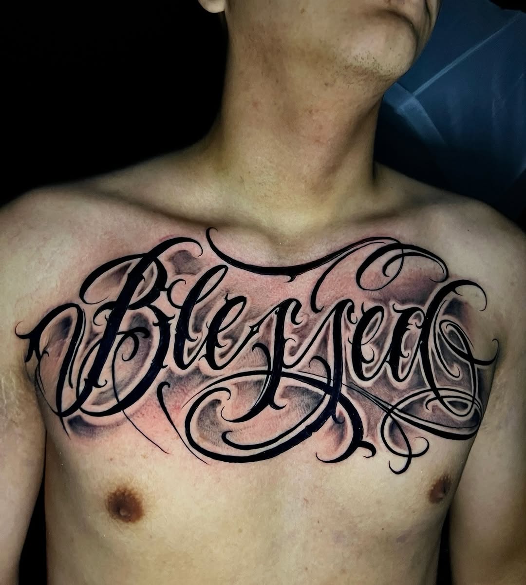 Script lettering Chicano tattoo on the chest by El Salvador Tattoo Artist