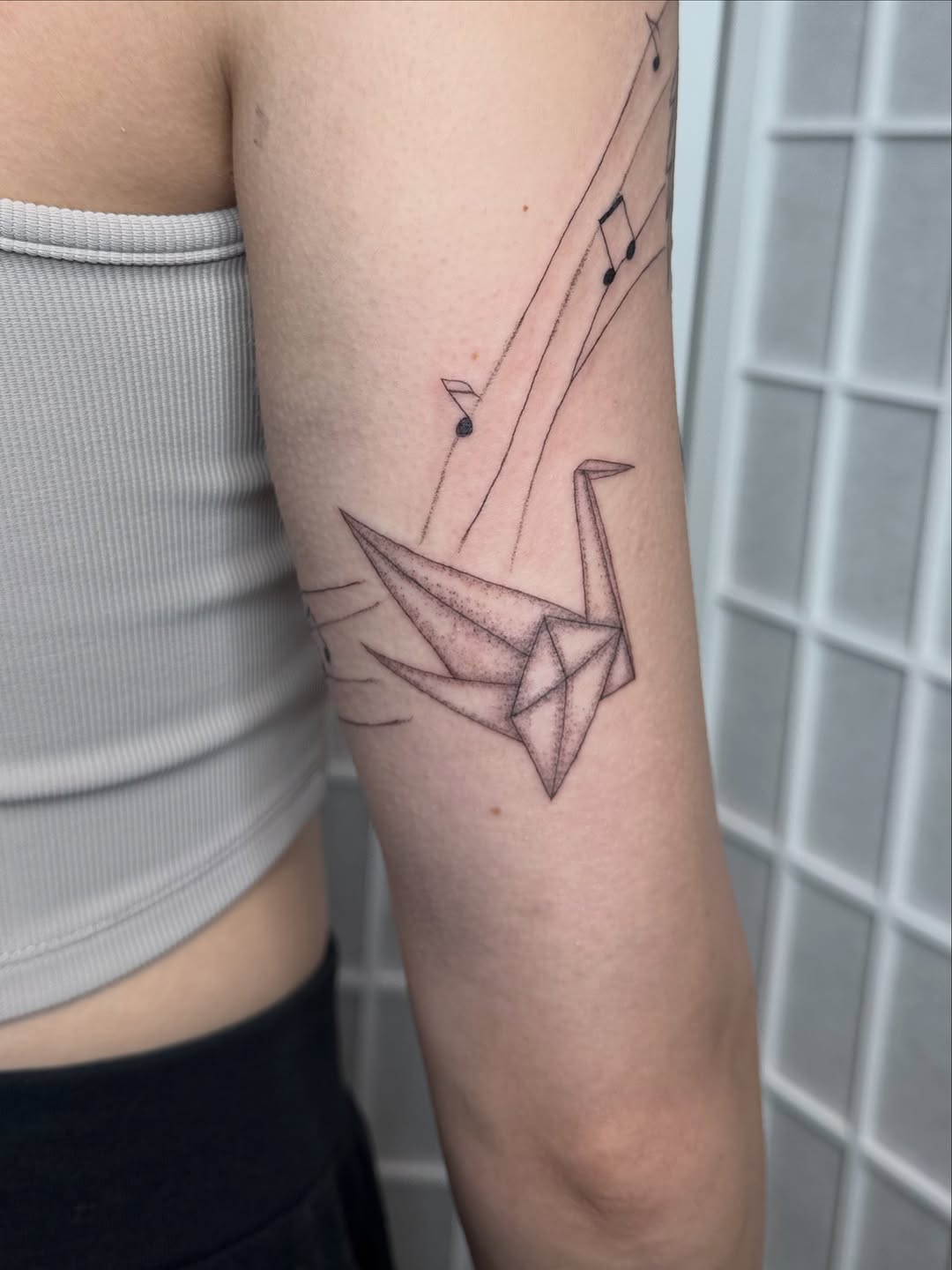 Origami crane and musical notes fine line tattoo on the forearm by Dama