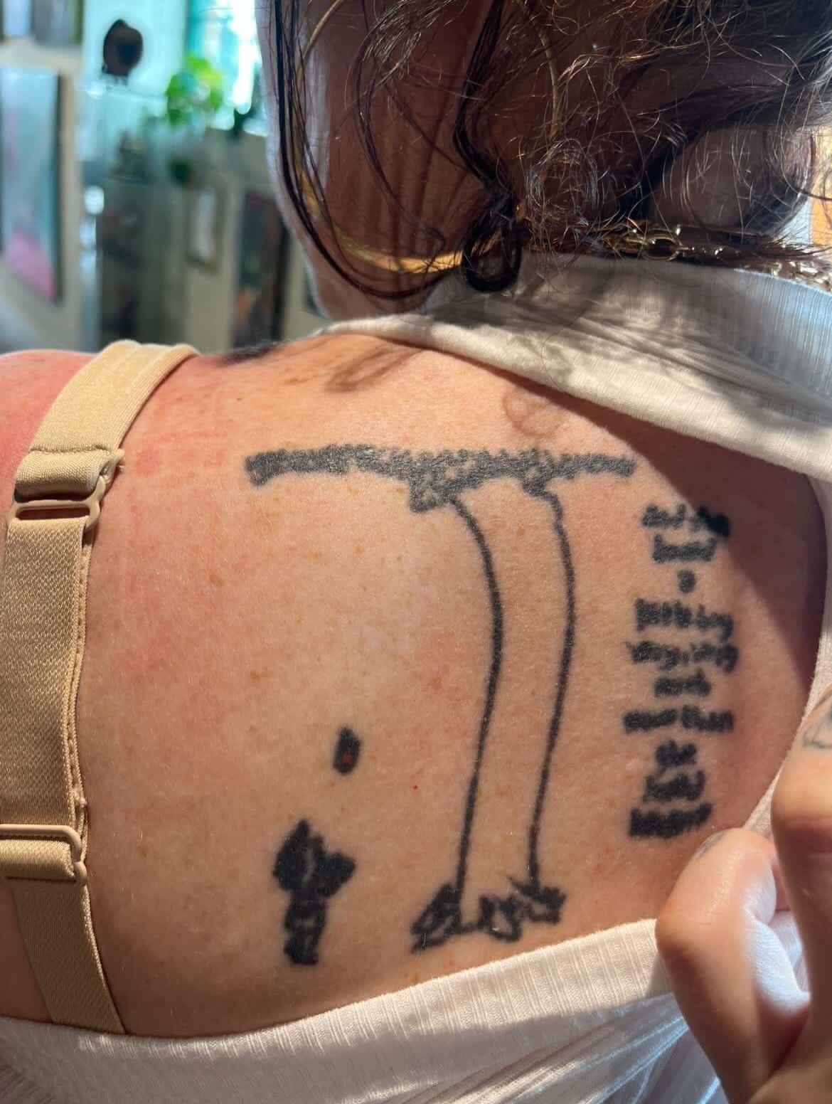 Man with fishing pole black and grey tattoo on the back by Elle Miller