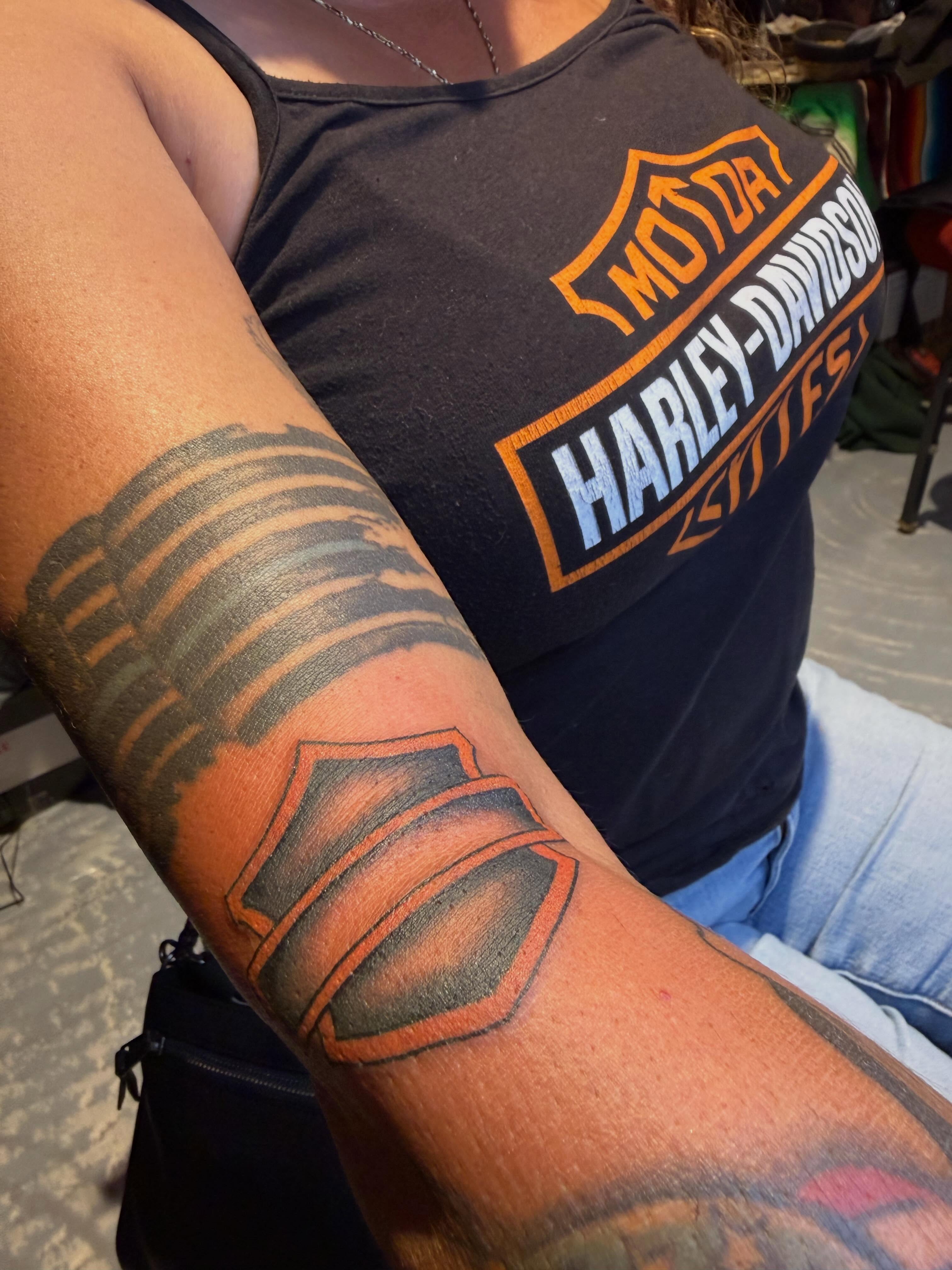 Motorcycle shield black and grey tattoo on the forearm by Chris de Armas