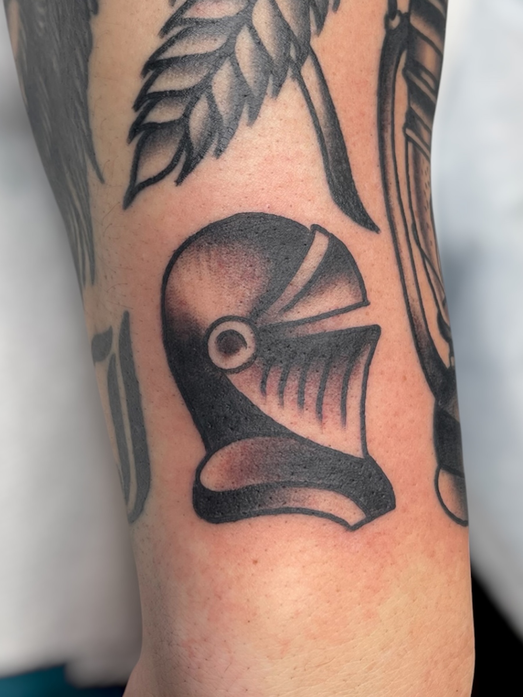 Helmet black and grey tattoo on the forearm by Chris Martin