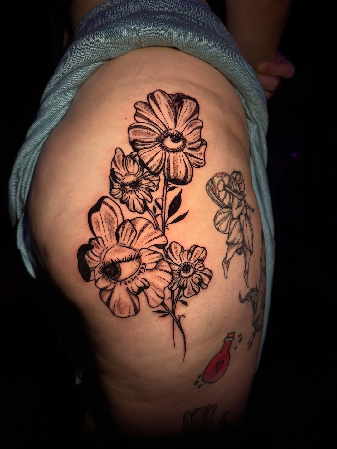 Flowers with eyes ignorant tattoo on the thigh by licensed charlotte tattoo artist