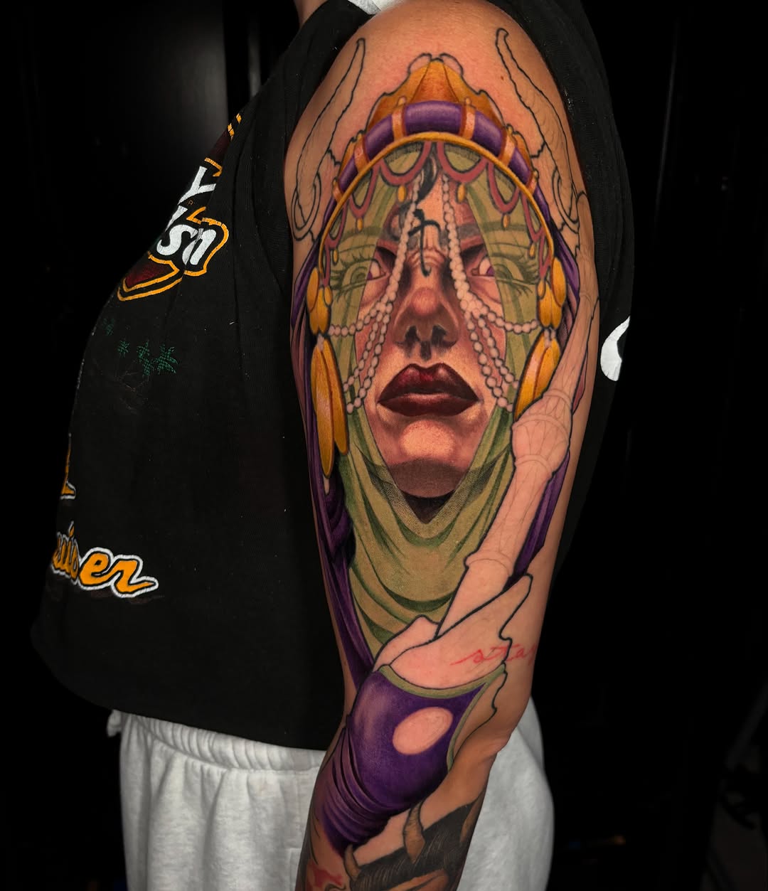 Woman with ornate headdress realism tattoo on the upper arm by Jon Ronzka
