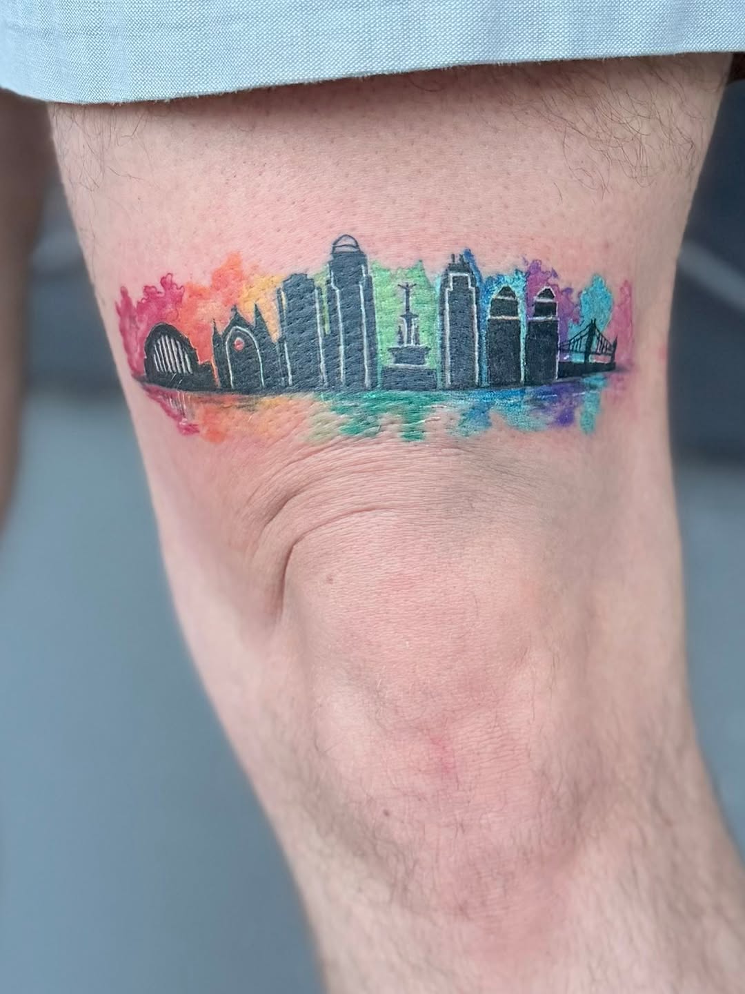 City skyline with rainbow watercolor background watercolor tattoo on the thigh by Gisette Gomez