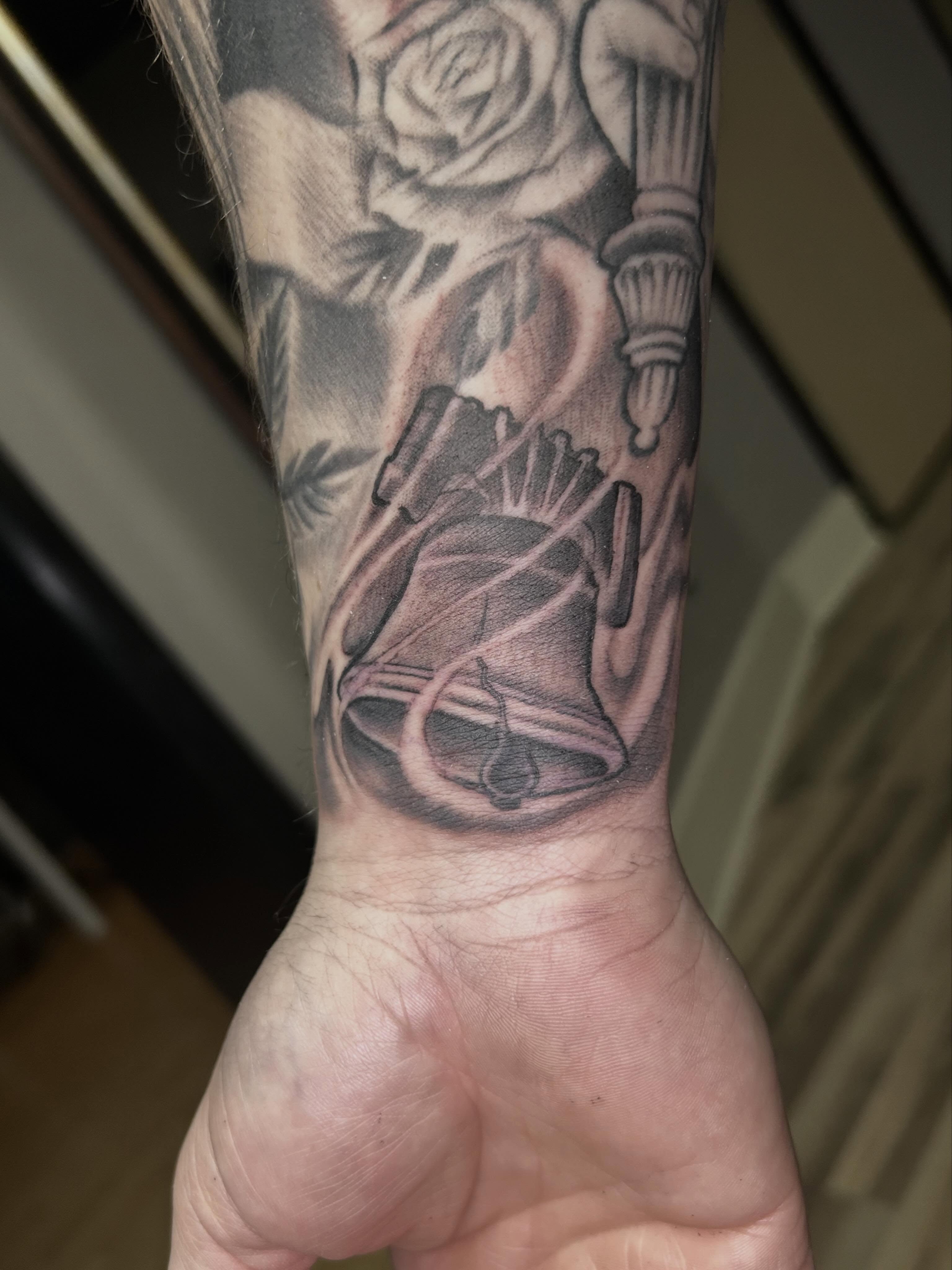 Bell and rose realism tattoo on the forearm by Dan Schuster