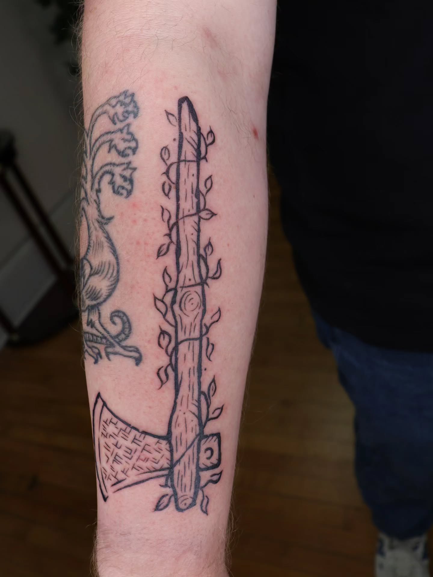 Axe and tree trunk black and grey tattoo on the forearm by Veronika Lipchak