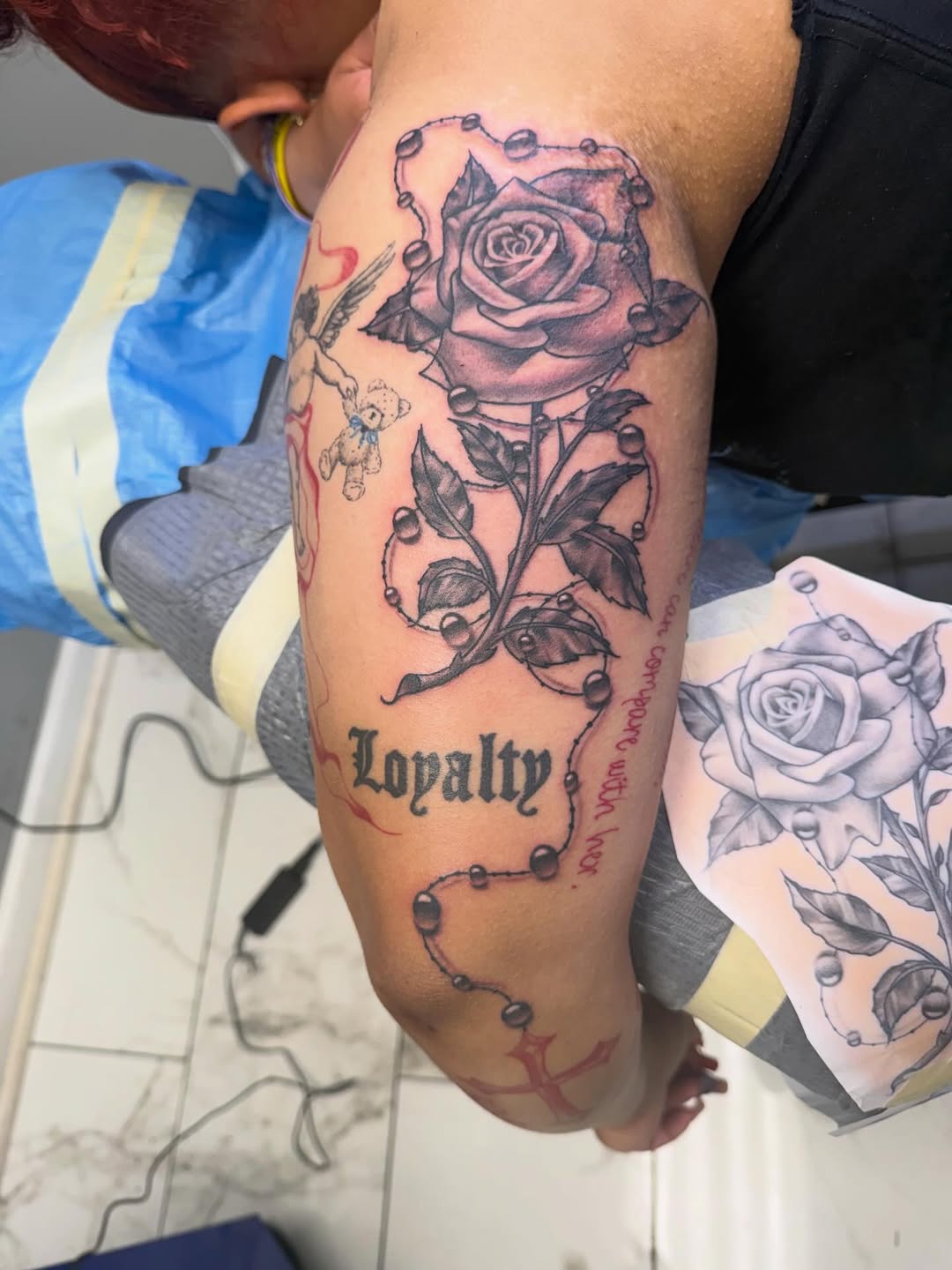 Rose with rosary beads and lettering Chicano tattoo on the forearm by linda perez