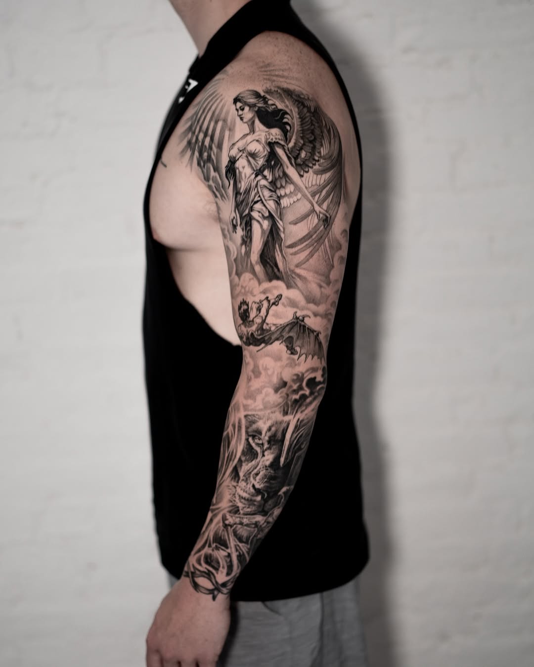 Angel and falling figure, lion realism tattoo on the upper arm by Mark Vata