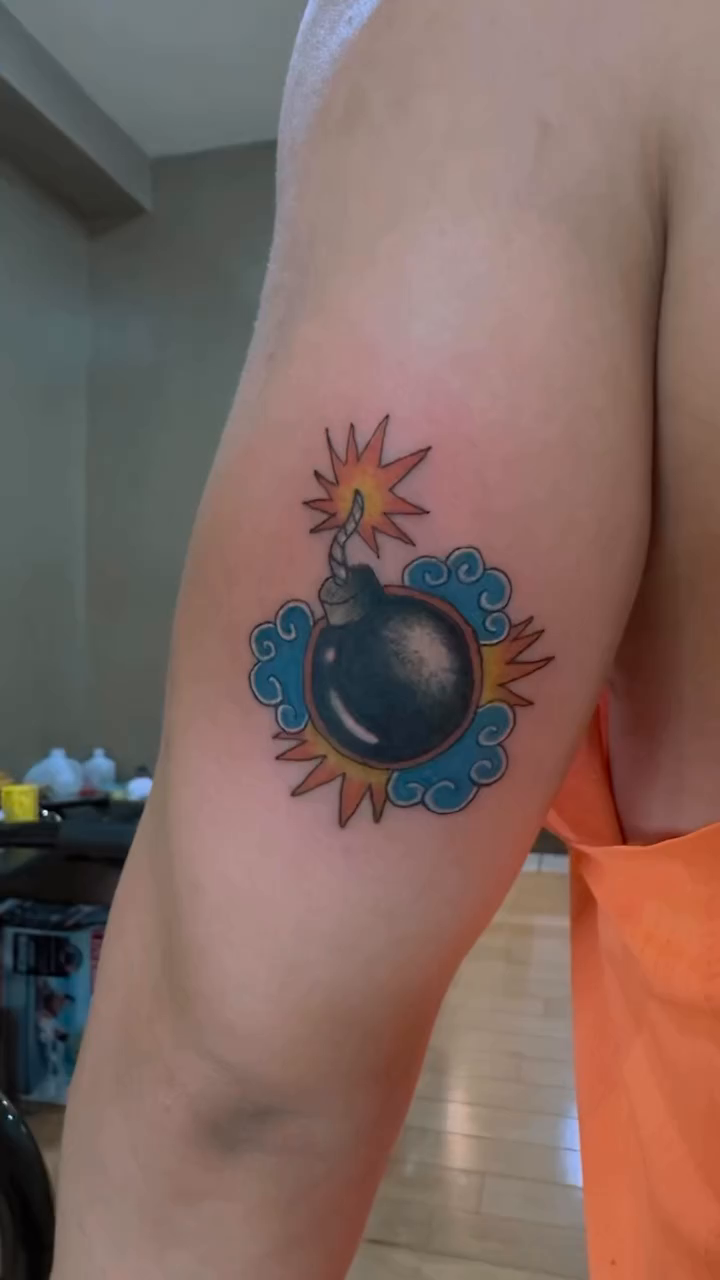 Bomb with fuse and stylized clouds new school tattoo on the forearm by Ink Napawong