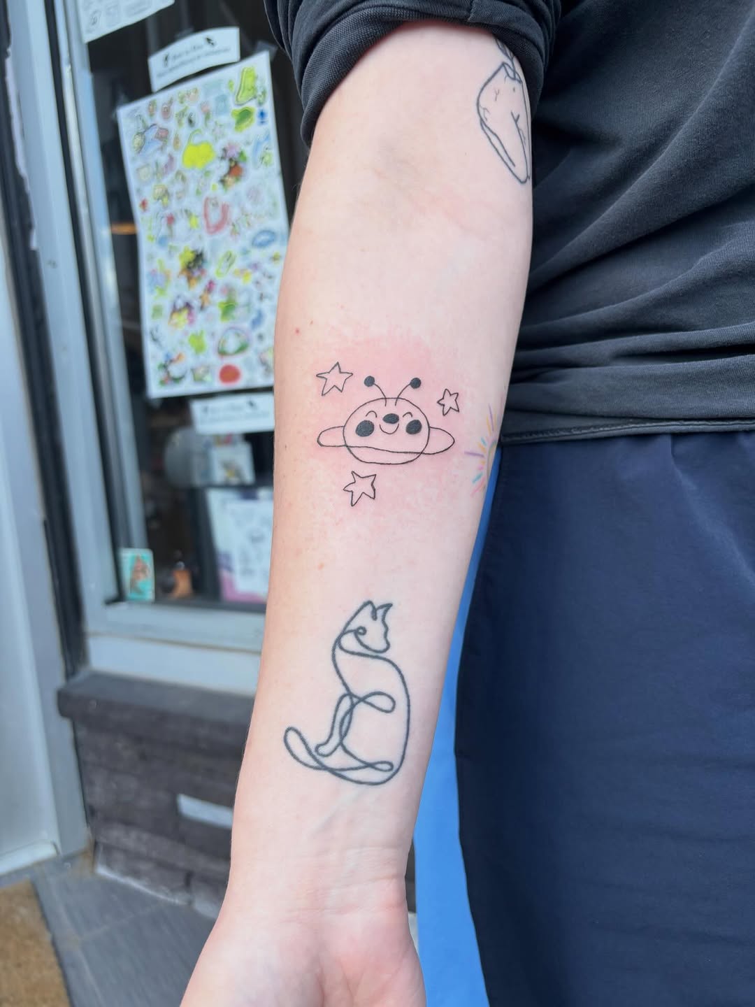 Alien and cat minimalist tattoo on the forearm by riley