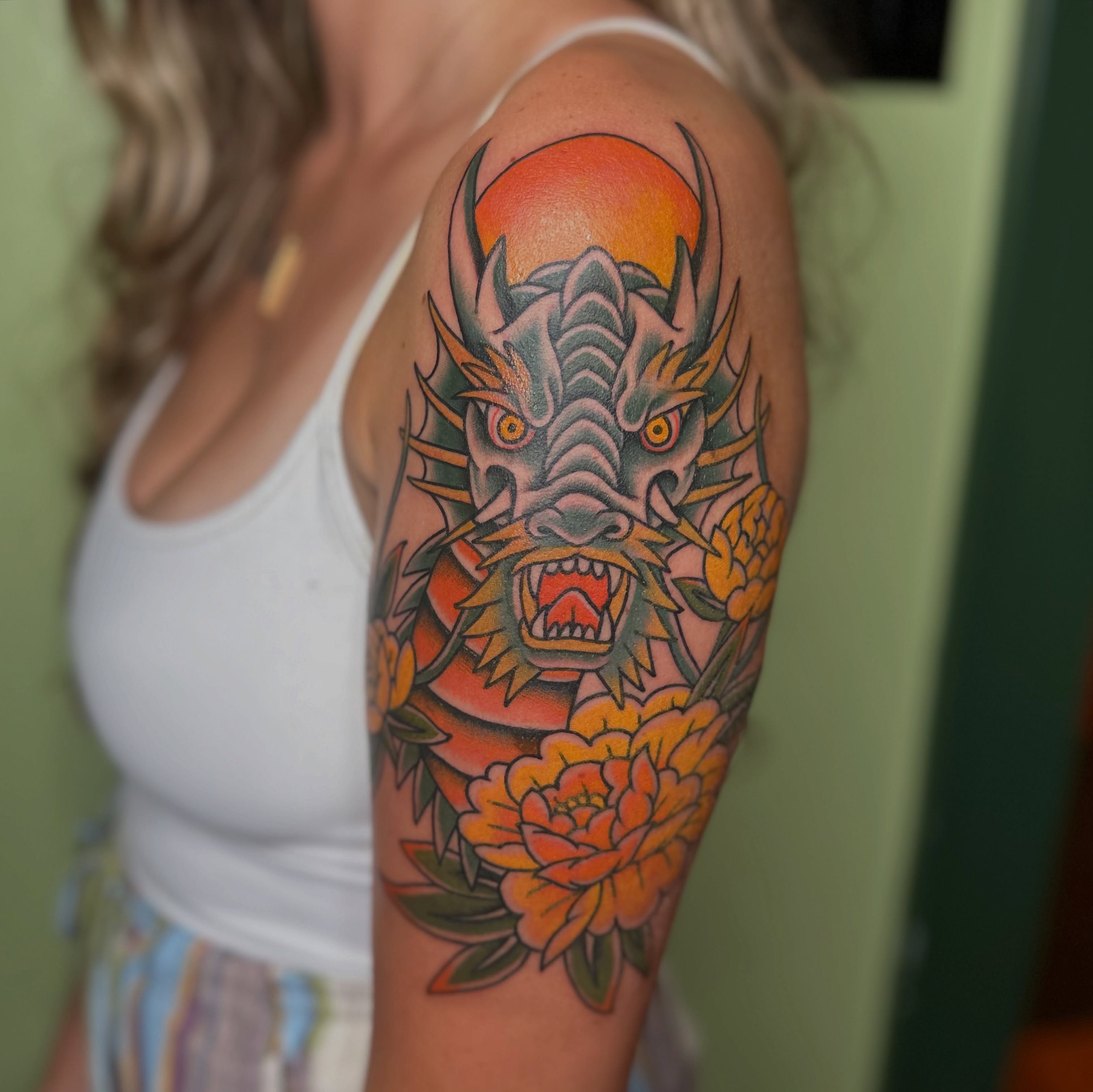 Dragon and flowers American traditional tattoo on the upper arm by Brieana Smith