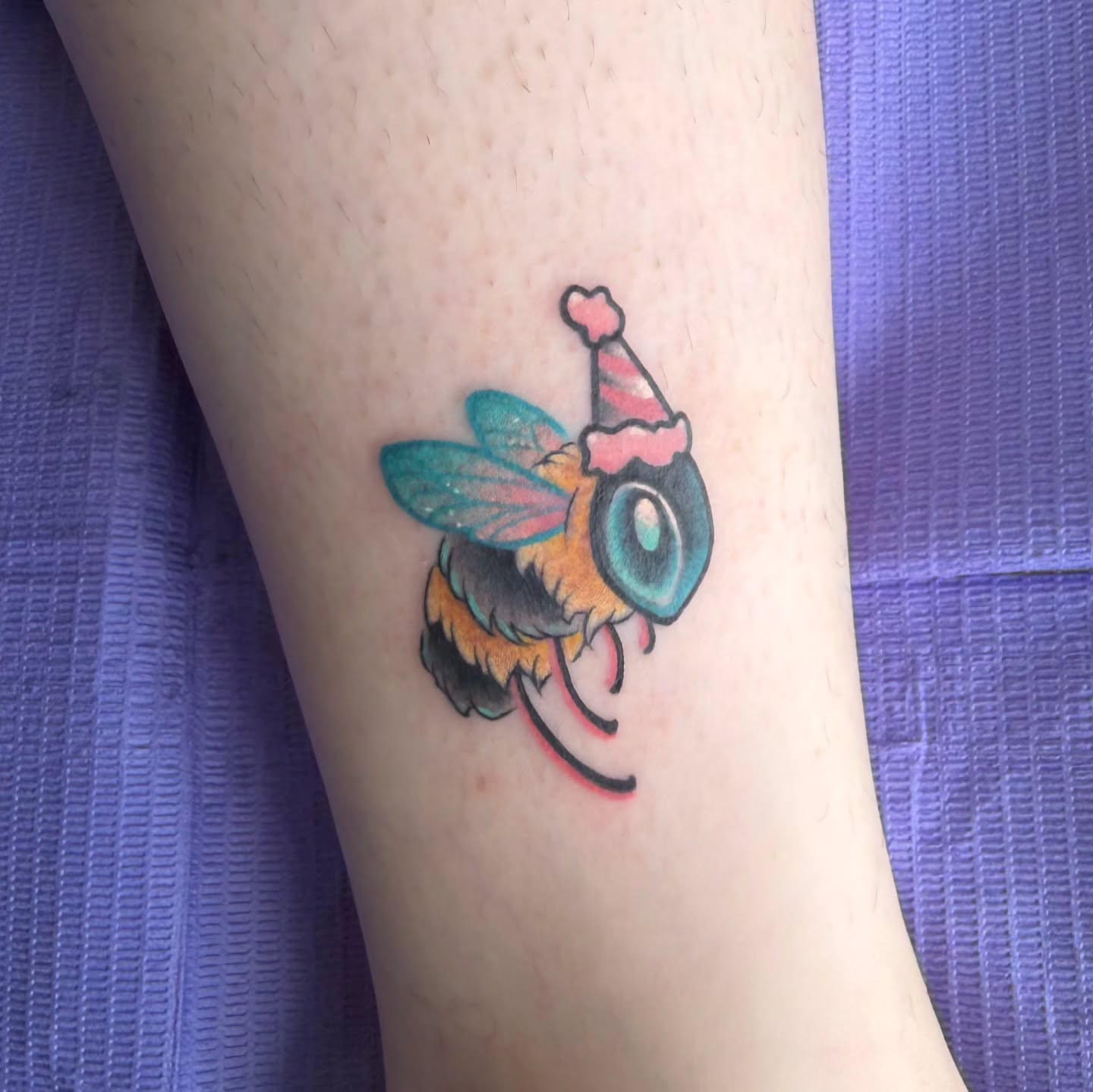 Bee wearing party hat new school tattoo on the forearm by Sam Castro