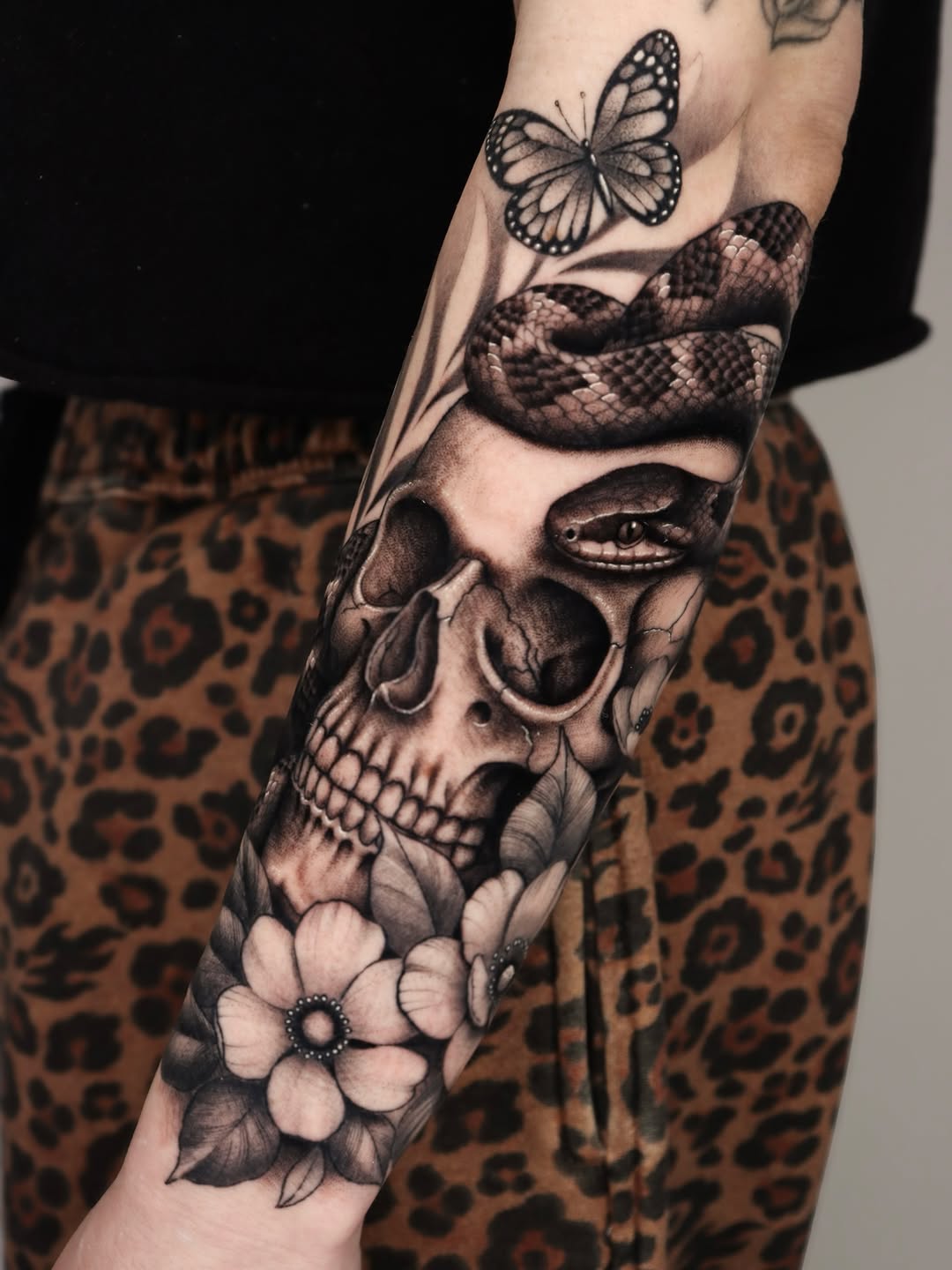 Skull with snake and flowers realism tattoo on the forearm by Jeff Reindel