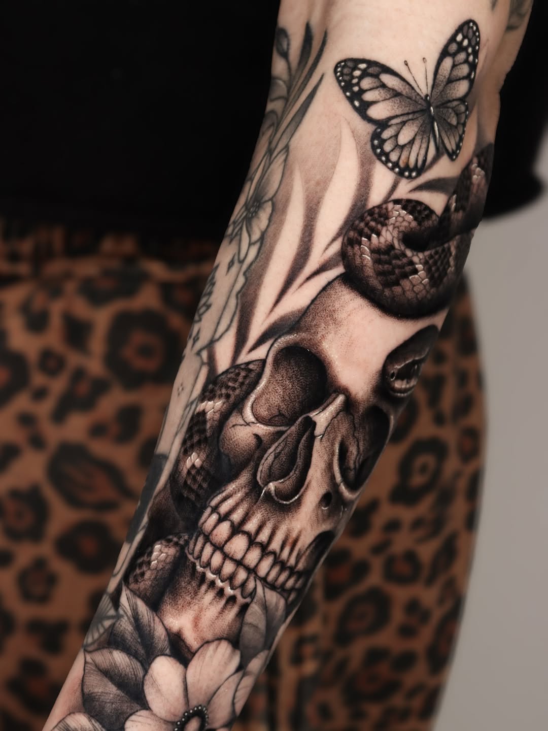 Skull, snake, butterfly, and flowers realism tattoo on the forearm by Jeff Reindel