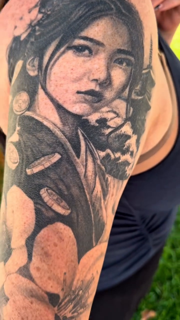 Portrait of a woman with flowers realism tattoo on the upper arm by Maggie George
