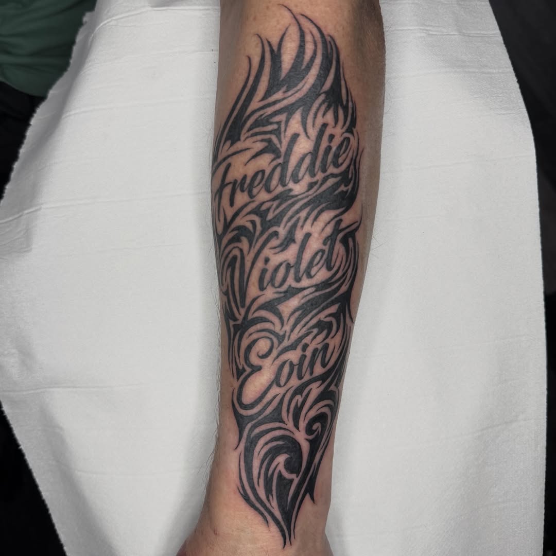 Flame and names tribal tattoo on the forearm by Aiden Shaw