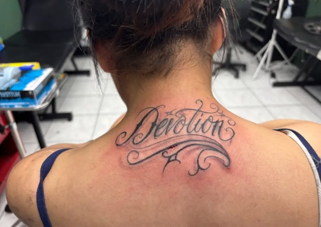 Script lettering 'Devotion' lettering tattoo on the neck by Shadows Tattoos