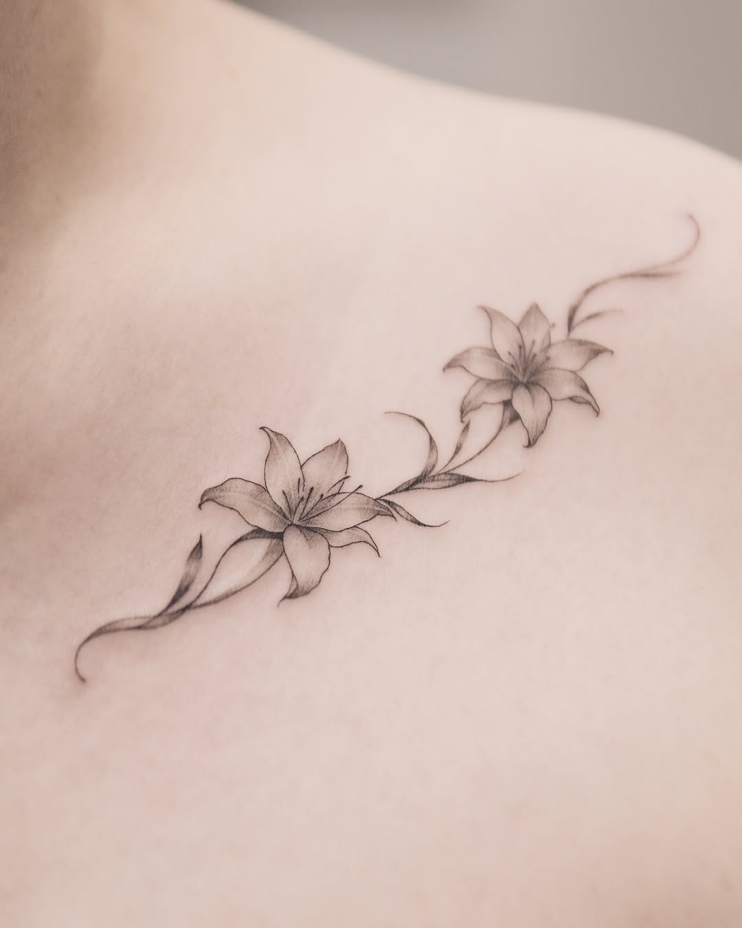 Two lilies on a vine fine line tattoo on the shoulder by Joey