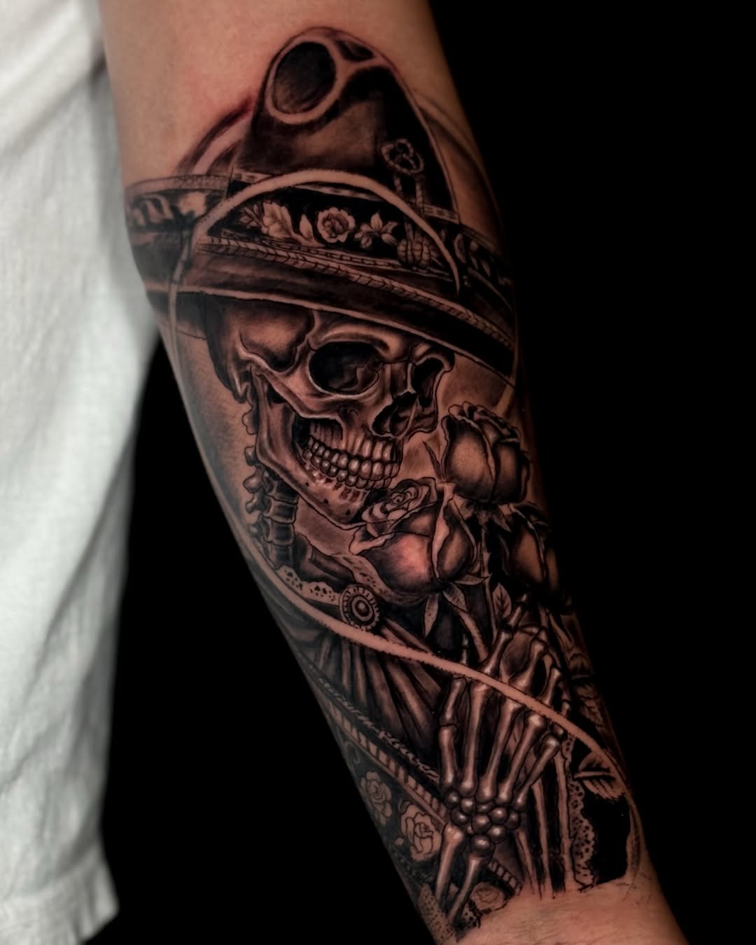 Skeleton with roses and hat realism tattoo on the forearm by German Patiño.