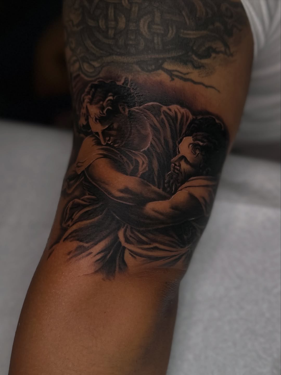 Two figures embracing realism tattoo on the forearm by Mando