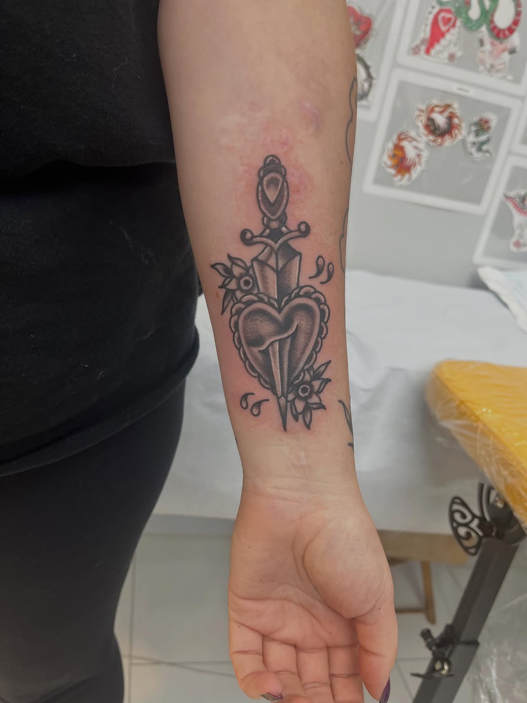 Dagger through heart with flowers American traditional tattoo on the forearm by Sour Tattoo, Somerville, Massachusetts