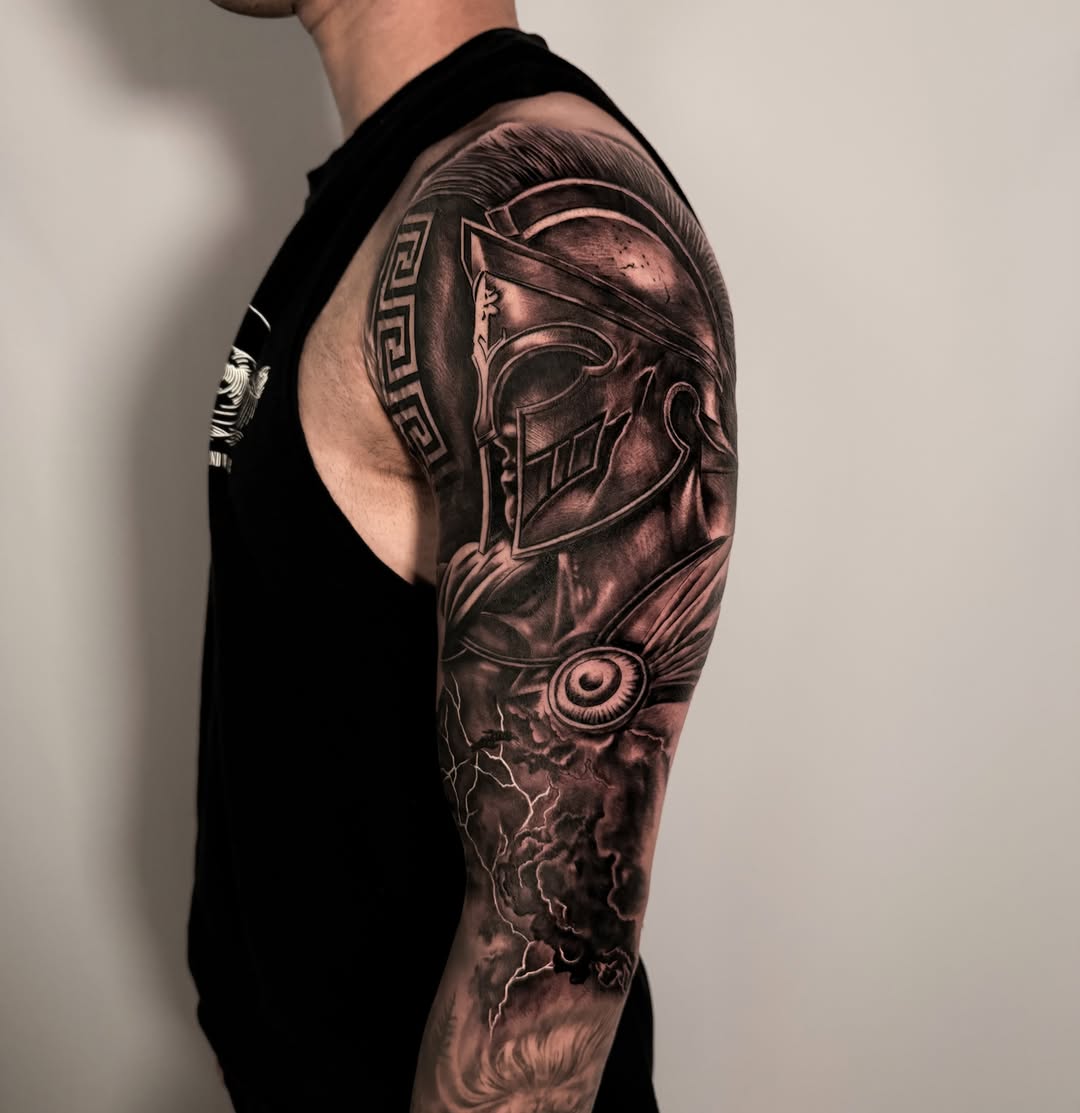 Spartan helmet with storm realism tattoo on the upper arm by Tattoos By Josh