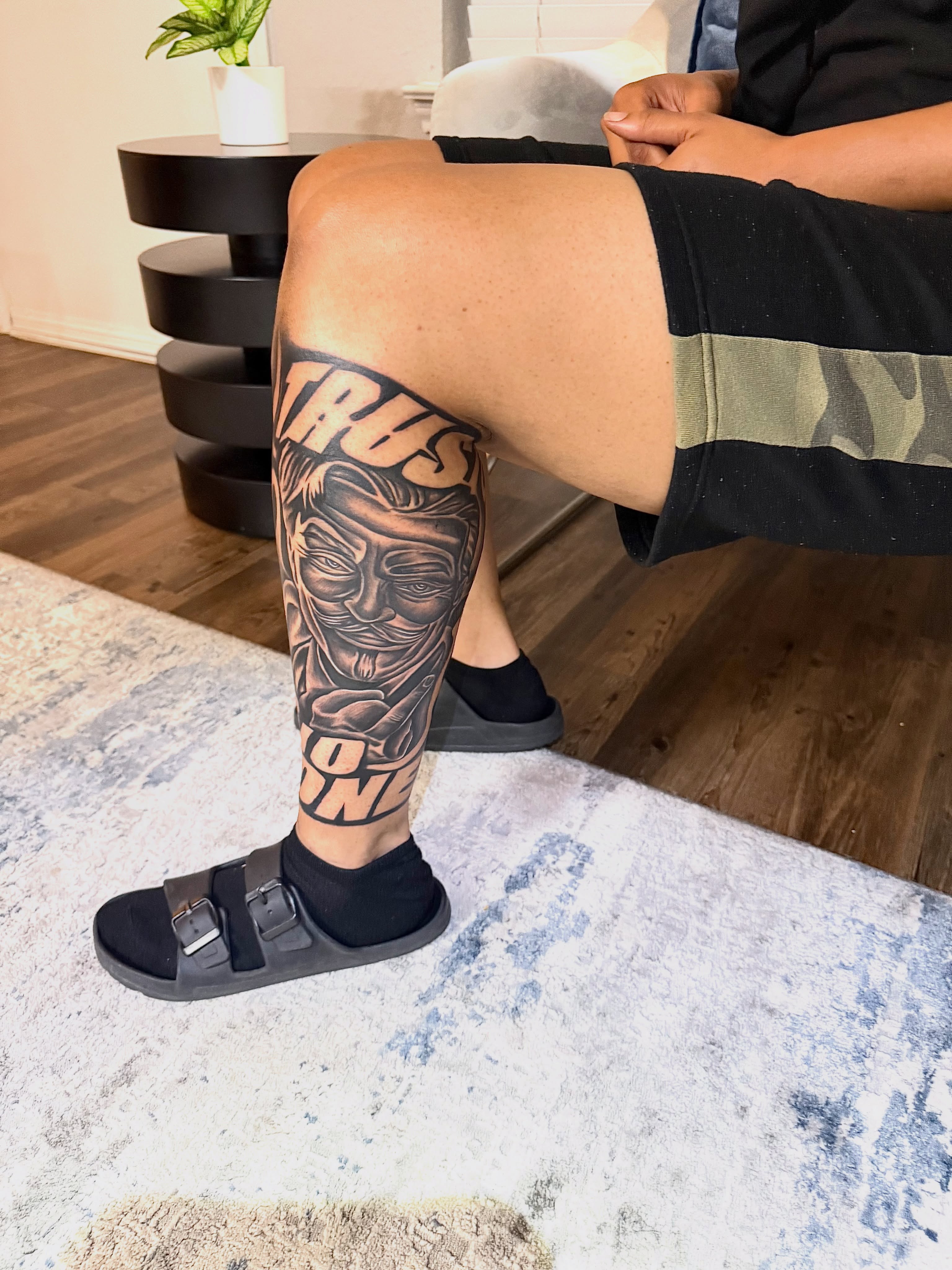 Mask and text black and grey tattoo on the calf by Deonte Dwayne Durham