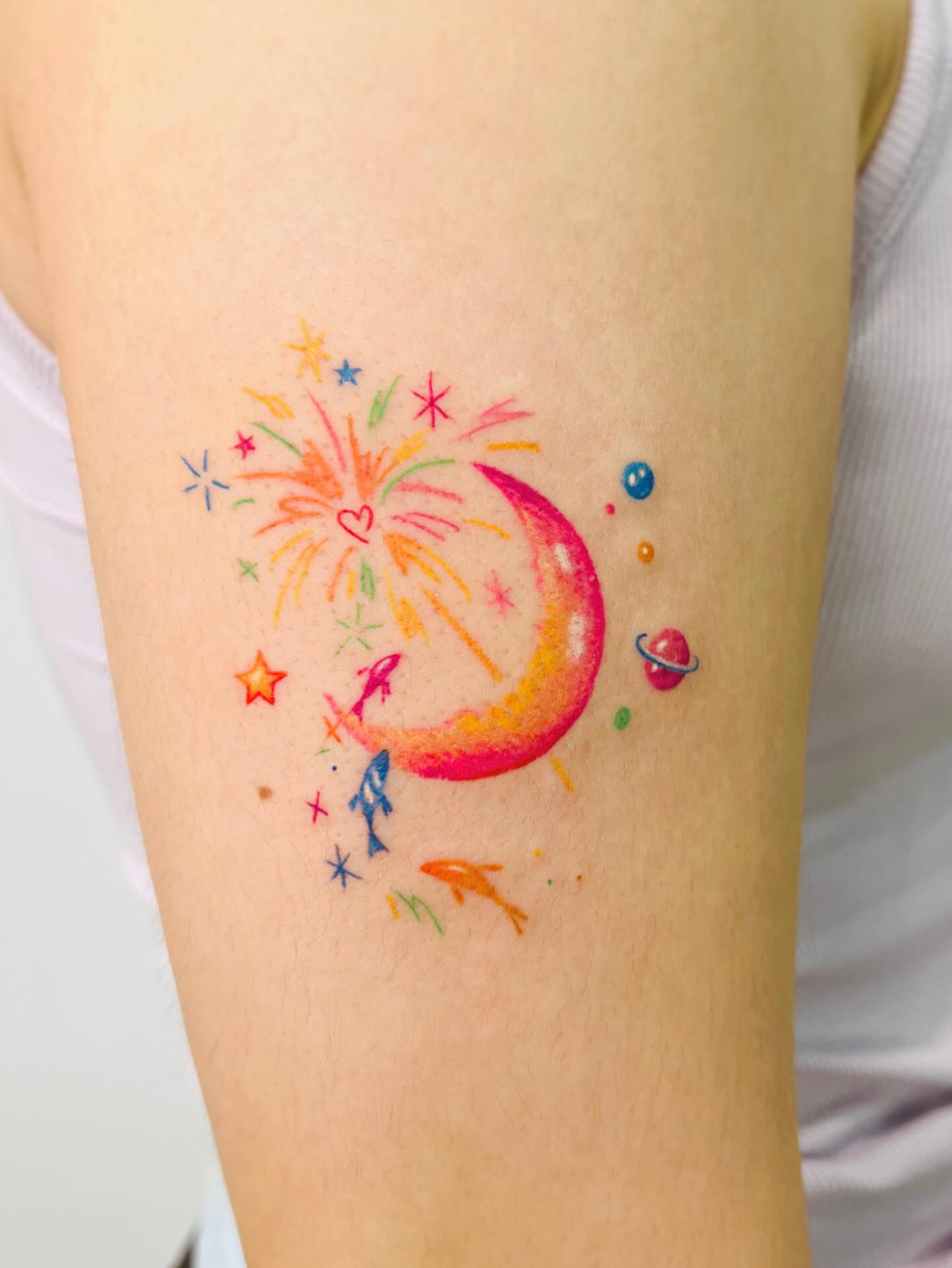 Space-themed crescent moon with fireworks watercolor tattoo on the forearm by Purinn