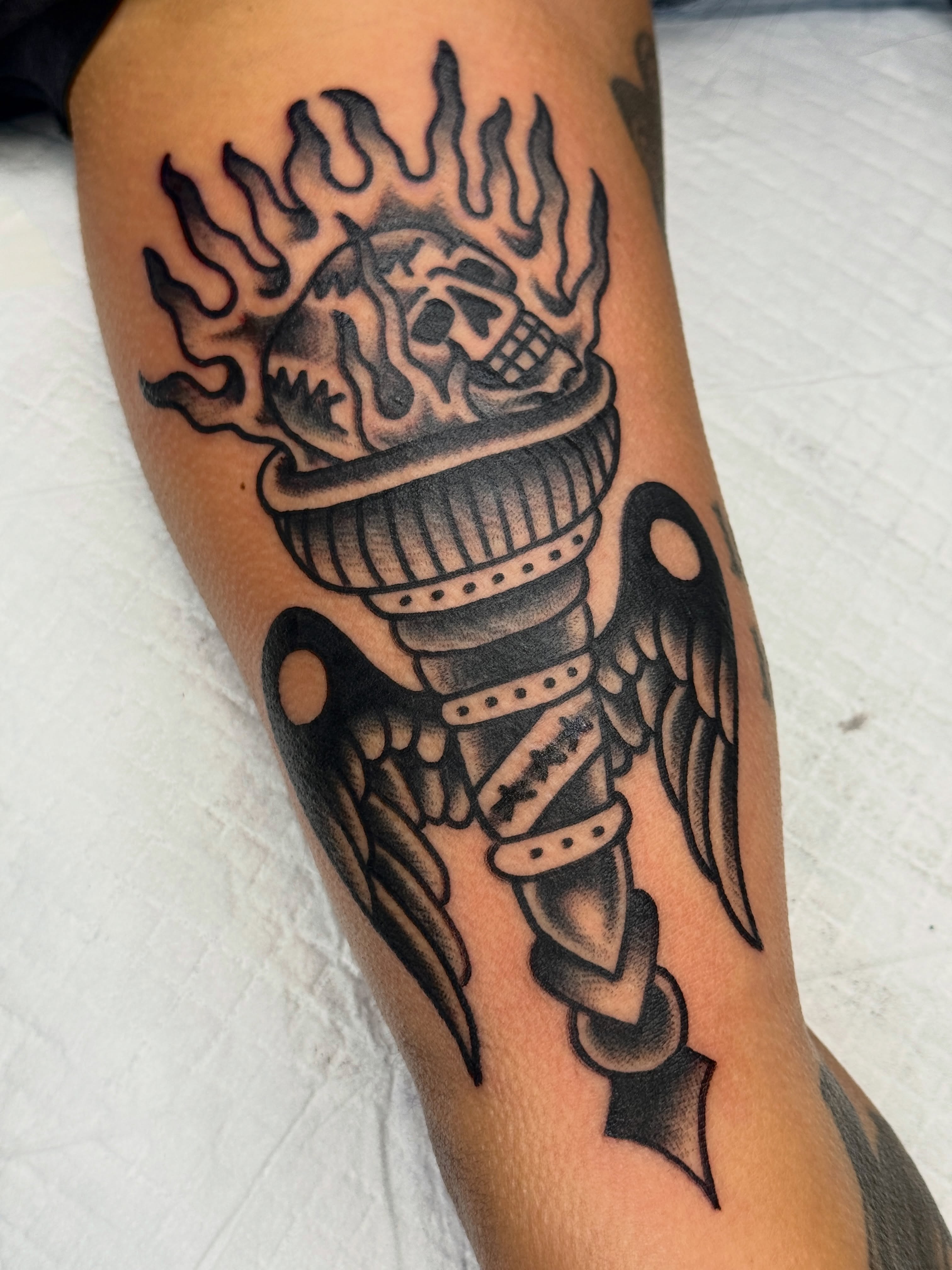 Flaming skull in urn black and grey tattoo on the forearm by Butch Mickle