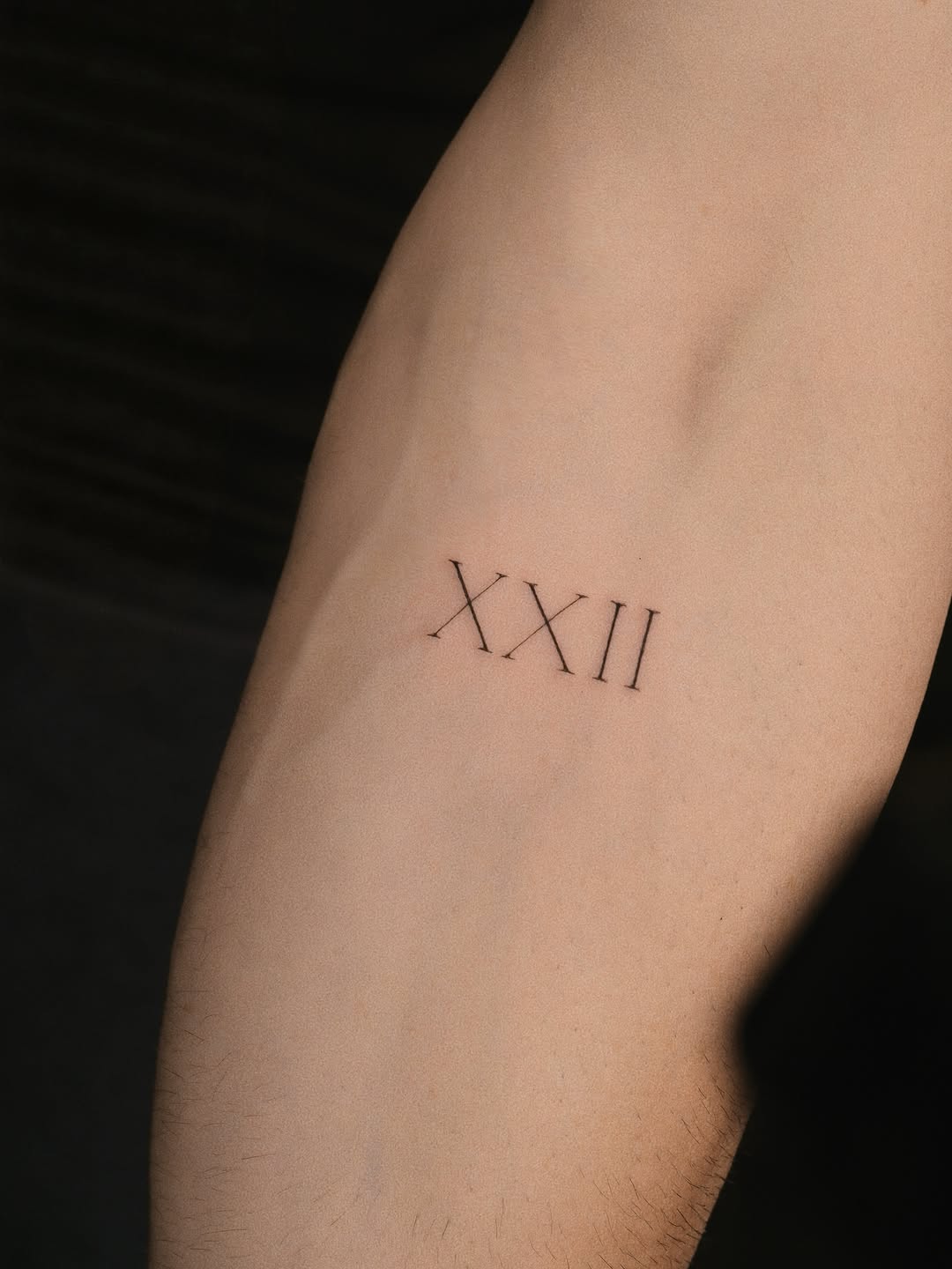 Roman numerals XXII fine line tattoo on the forearm by Victoria
