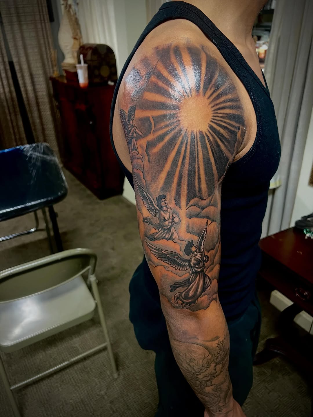 Sun with angels and clouds realism tattoo on the upper arm by Jelani