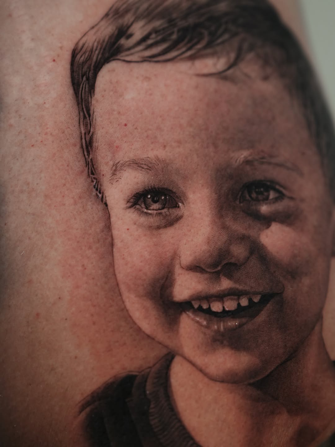 Child portrait realism tattoo on the upper arm by J O S S I e L P I N e D A