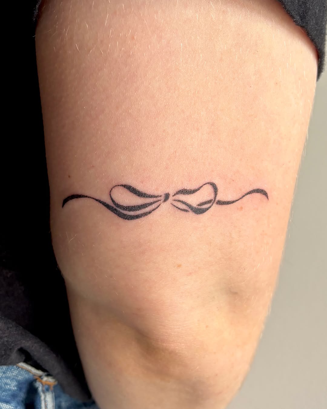 Bow with flourish minimalist tattoo on the forearm by alli ミ☆