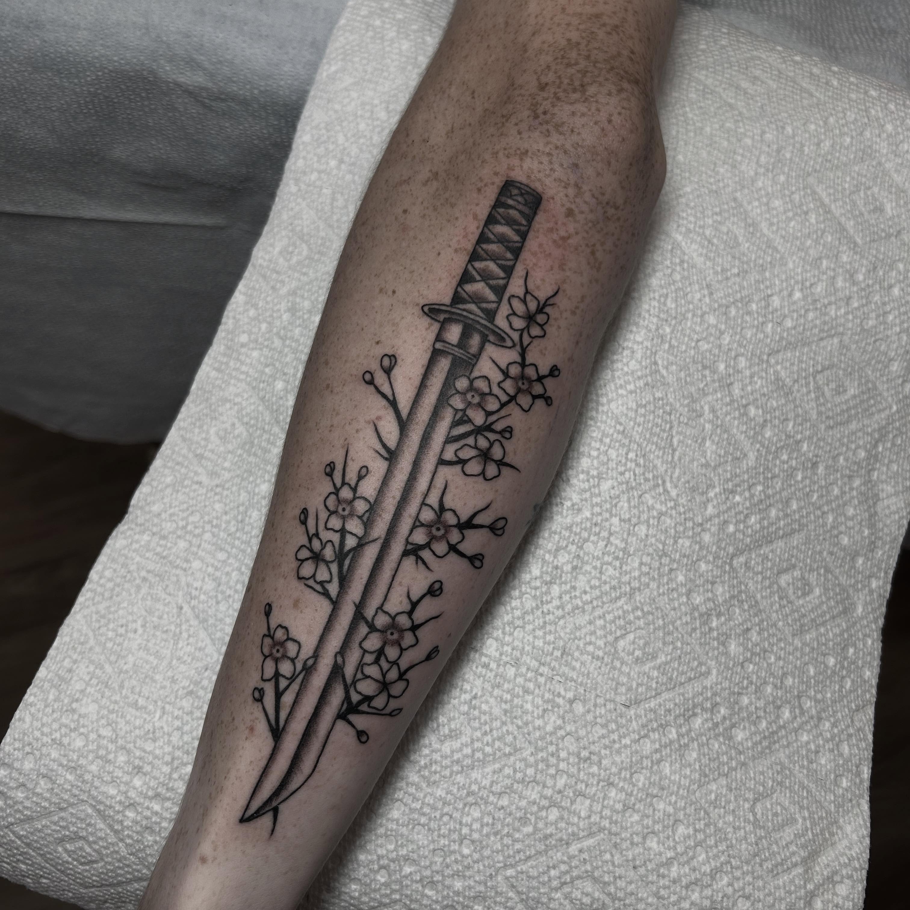 Katana and cherry blossoms black and grey tattoo on the forearm by Stephen Sanchez